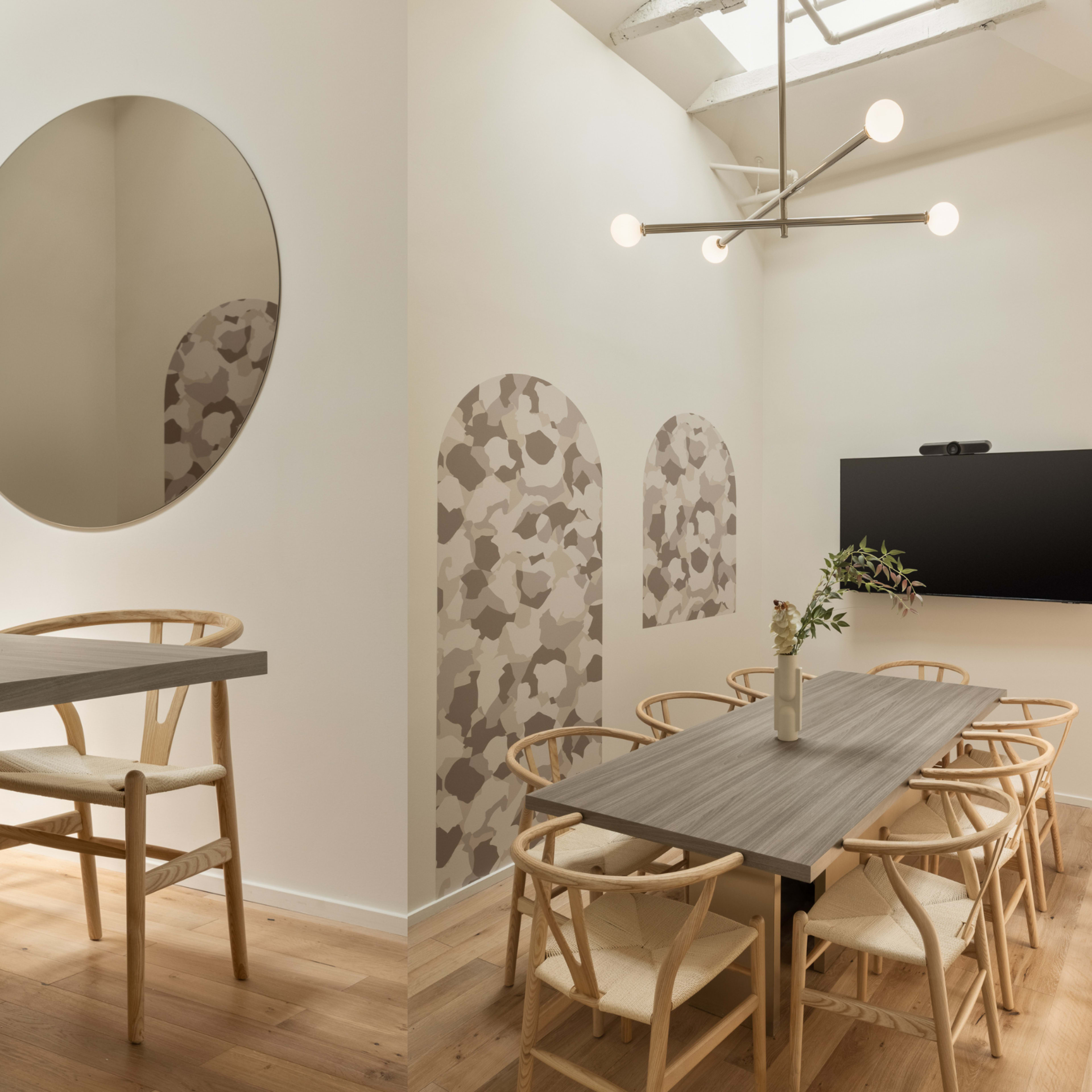 A modern dining area with a circular mirror, light wood floors, a large table surrounded by wooden chairs, and patterned wall decor.