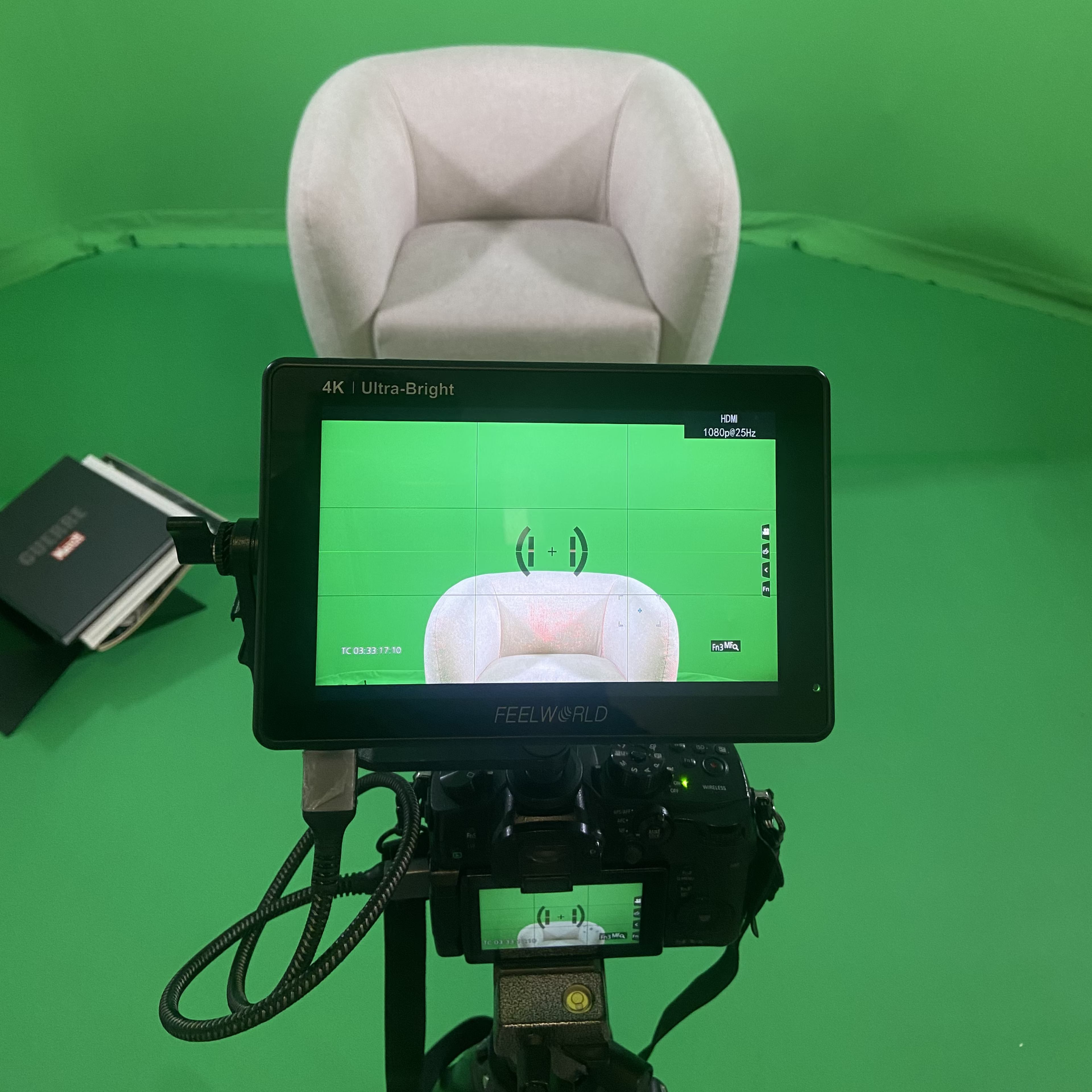 A camera setup focused on a gray chair in front of a green screen, with a monitor displaying the view.