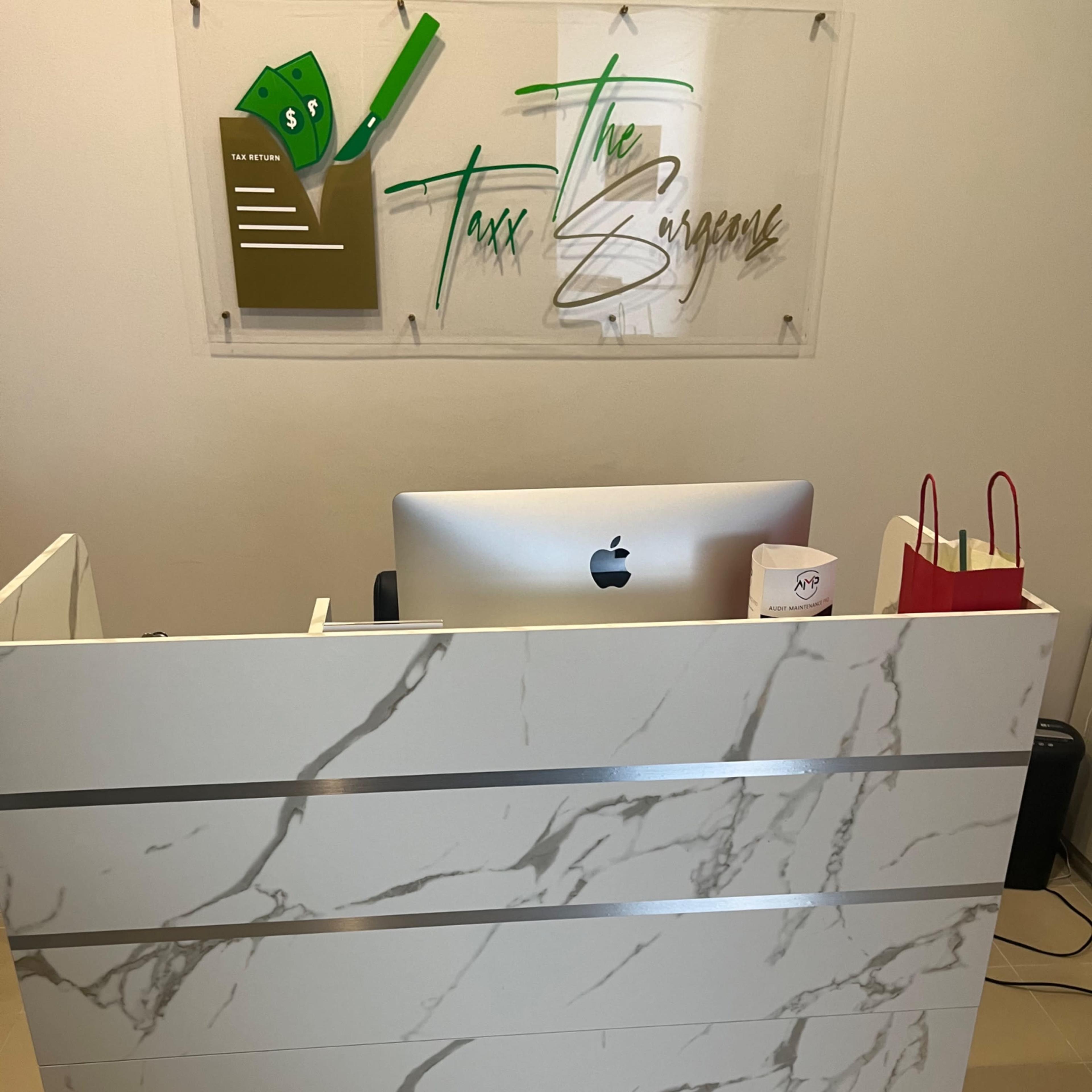 A modern reception desk with a marble design, positioned in front of a sign that reads "Taxx The Surgeons."