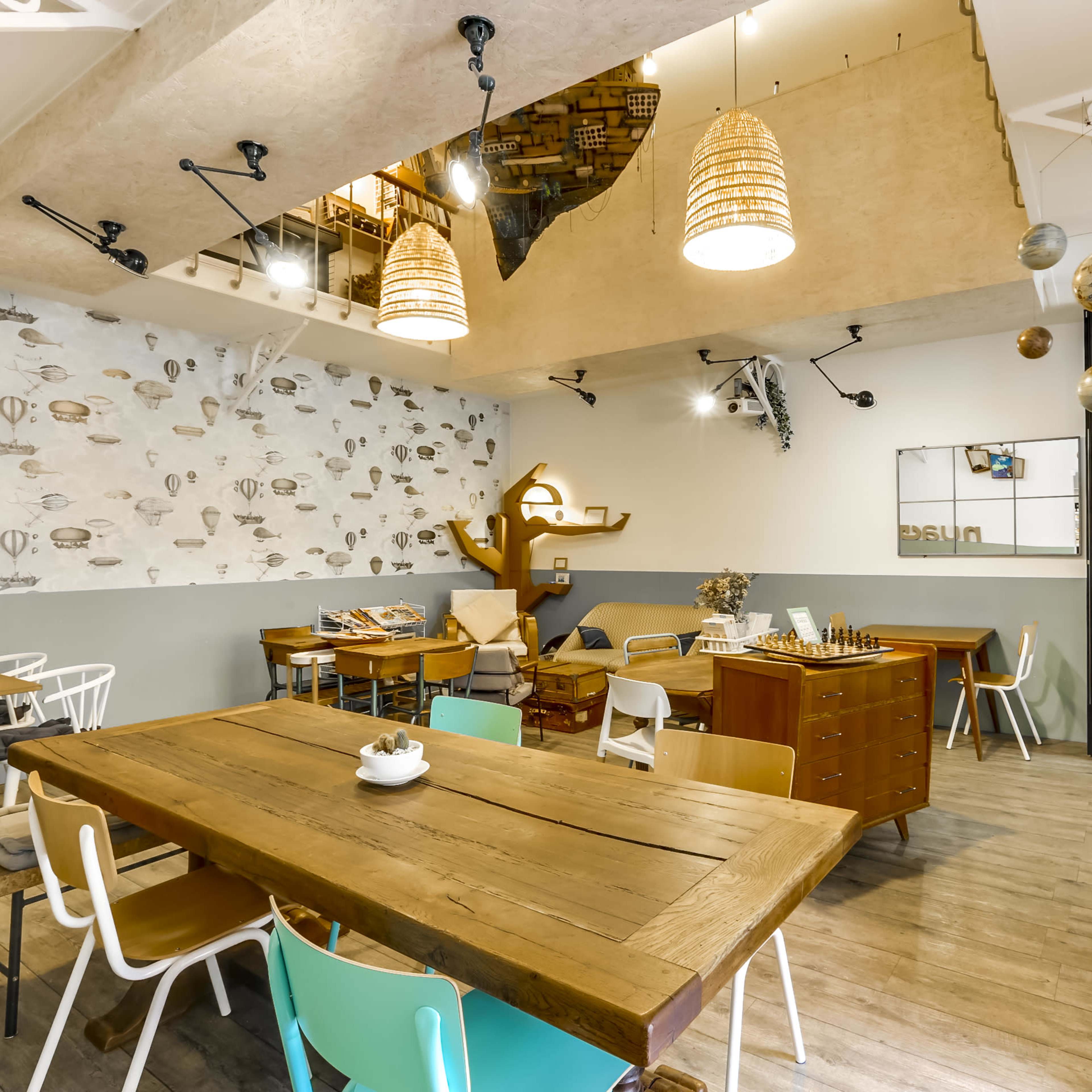 A cozy café interior featuring wooden tables, colorful chairs, and a staircase leading to an upper level decorated with books.