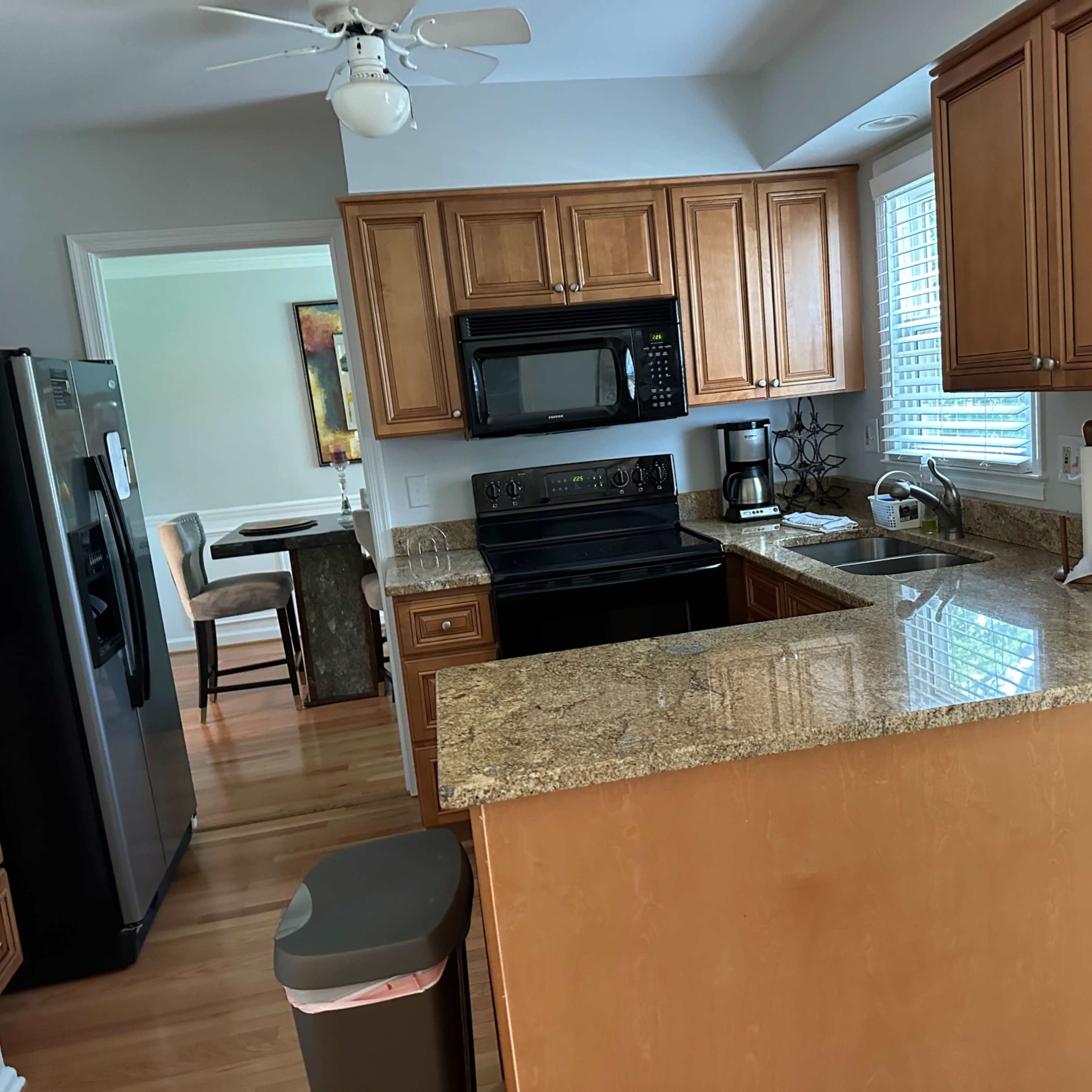 A spacious kitchen with wooden cabinetry, a black microwave and stove, and a granite countertop.