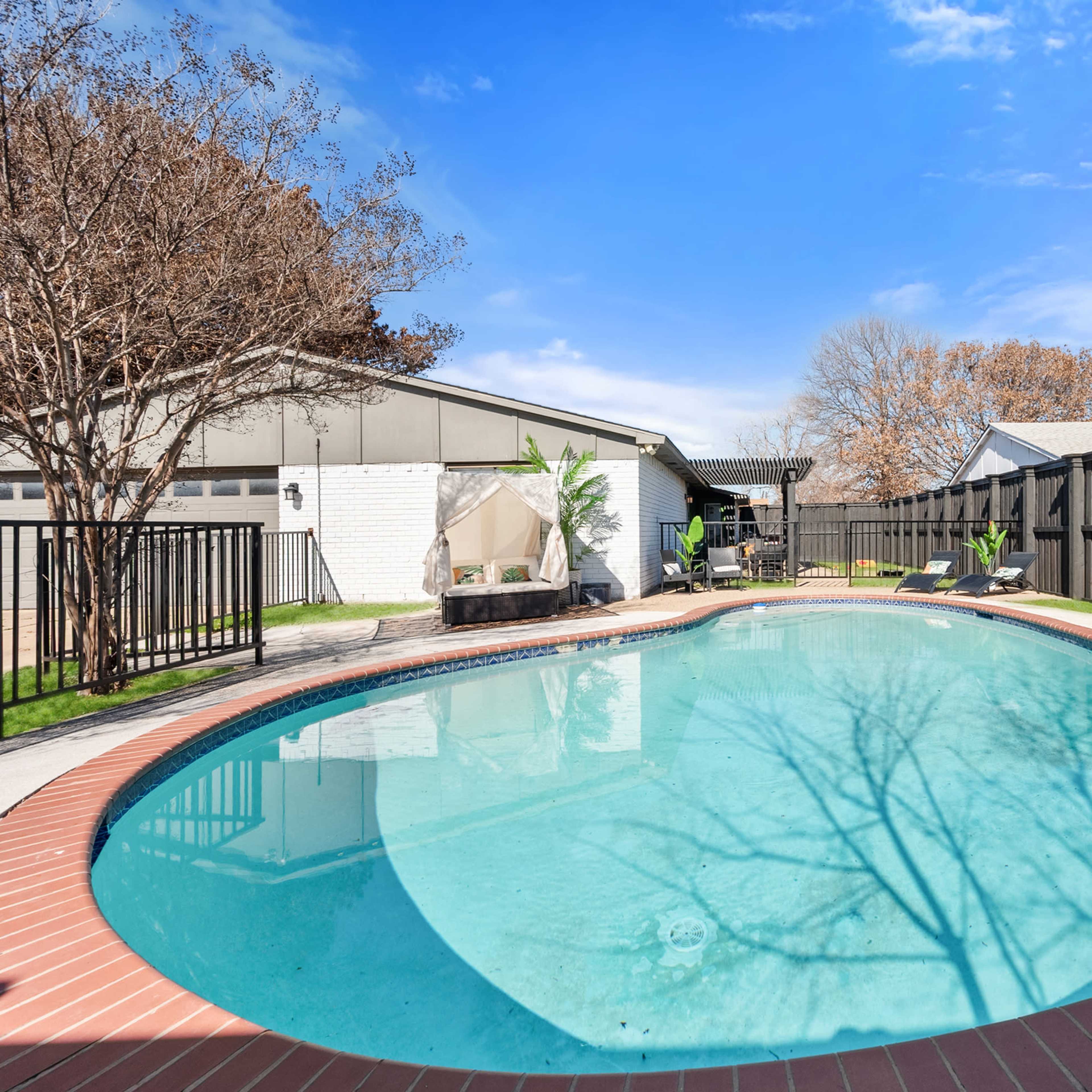A backyard features a swimming pool surrounded by a concrete patio and wooden fencing.