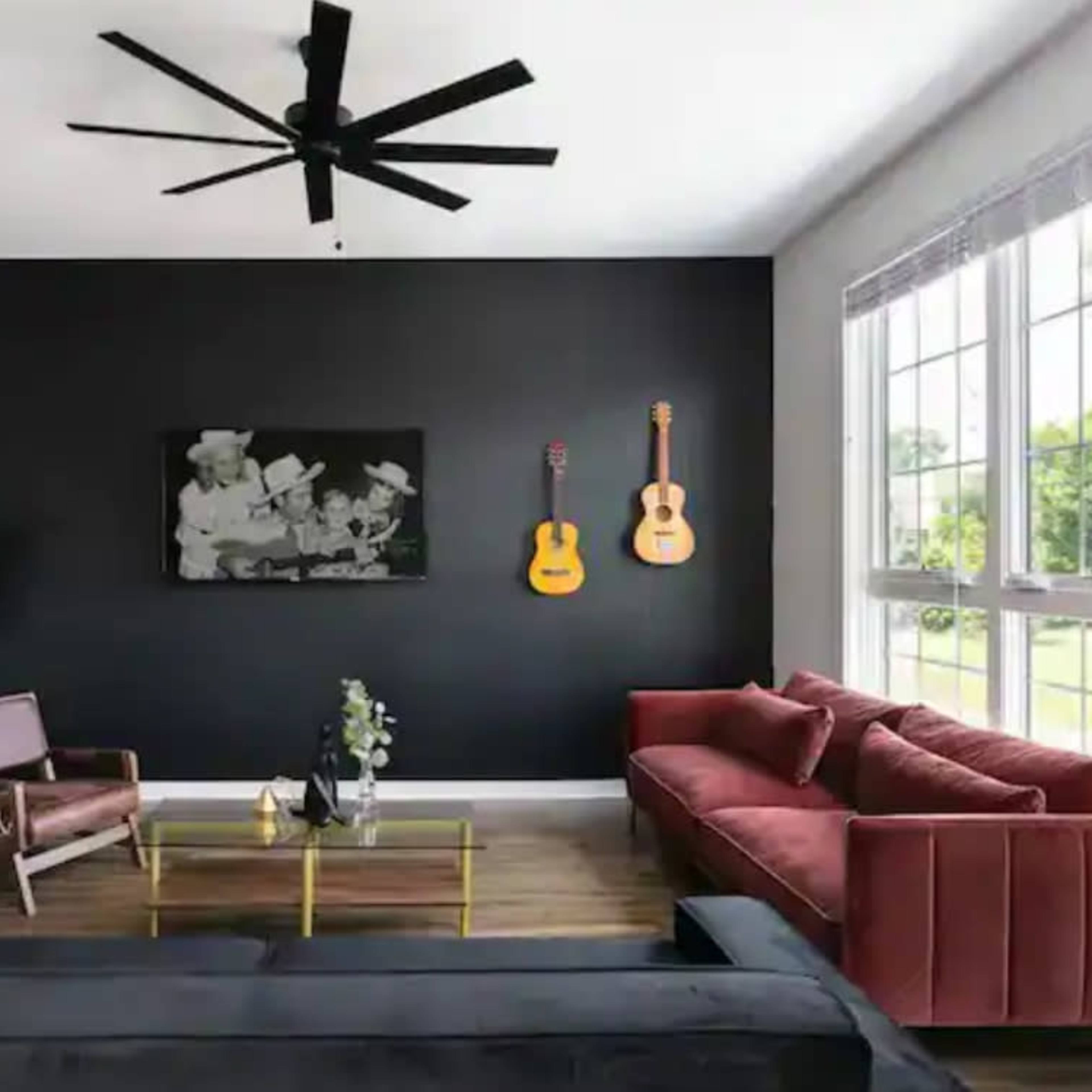 A modern living room features a dark accent wall with two acoustic guitars, a red sofa, a black sofa, a wooden coffee table, and large windows allowing natural light.