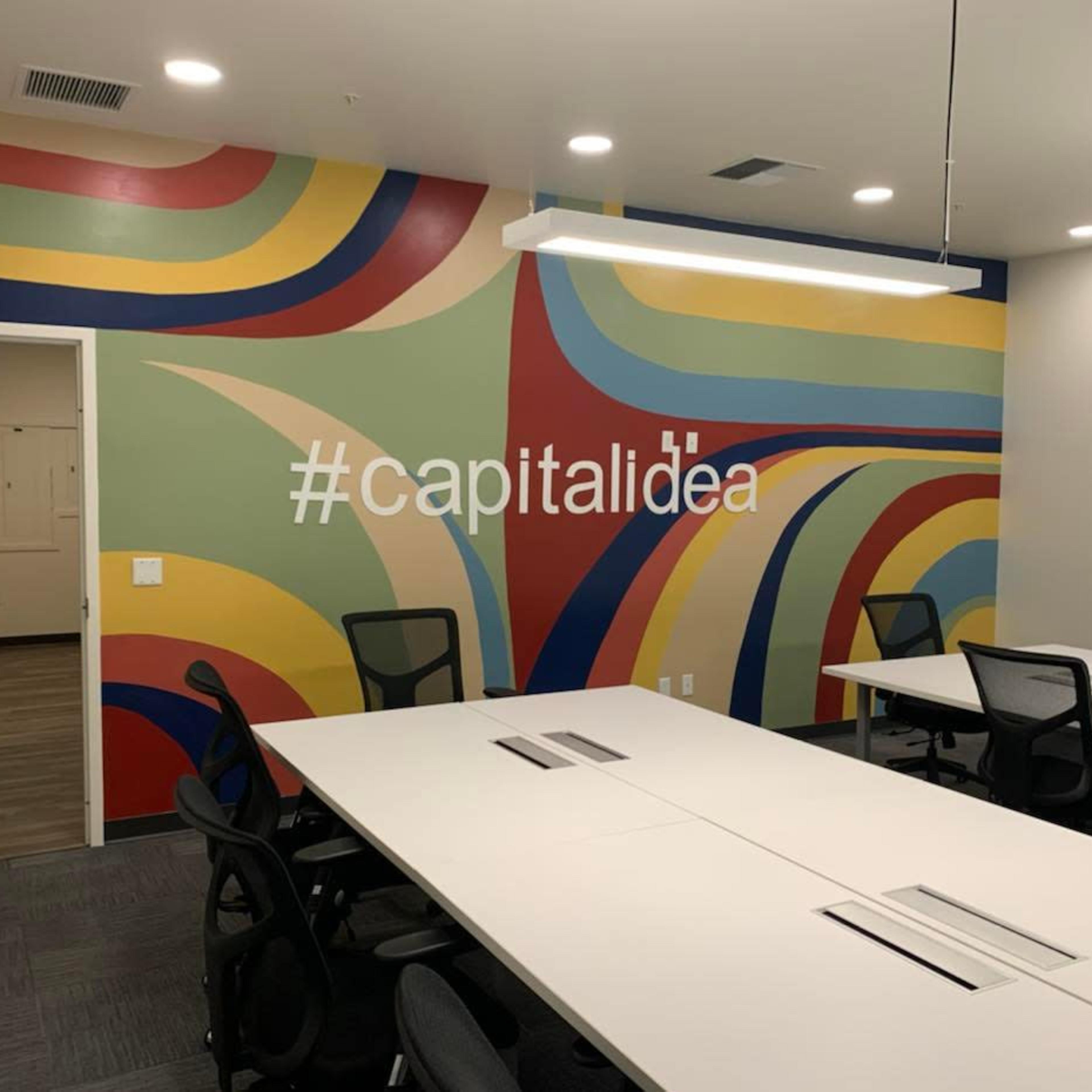A conference room featuring a multicolored abstract mural on one wall and a long white table with black chairs.