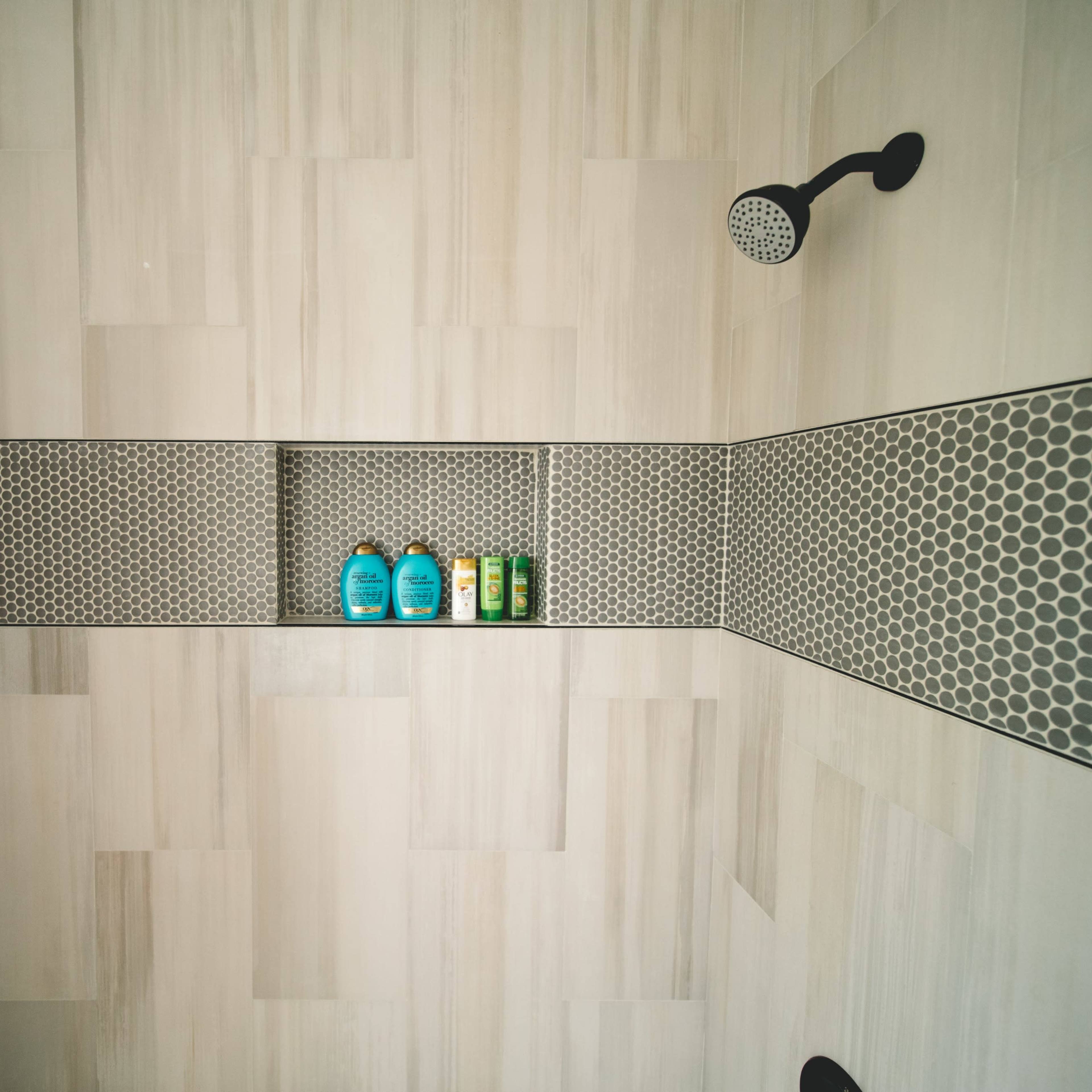A modern shower with a wall-mounted showerhead and a shelf containing three bottles of shampoo or body wash.