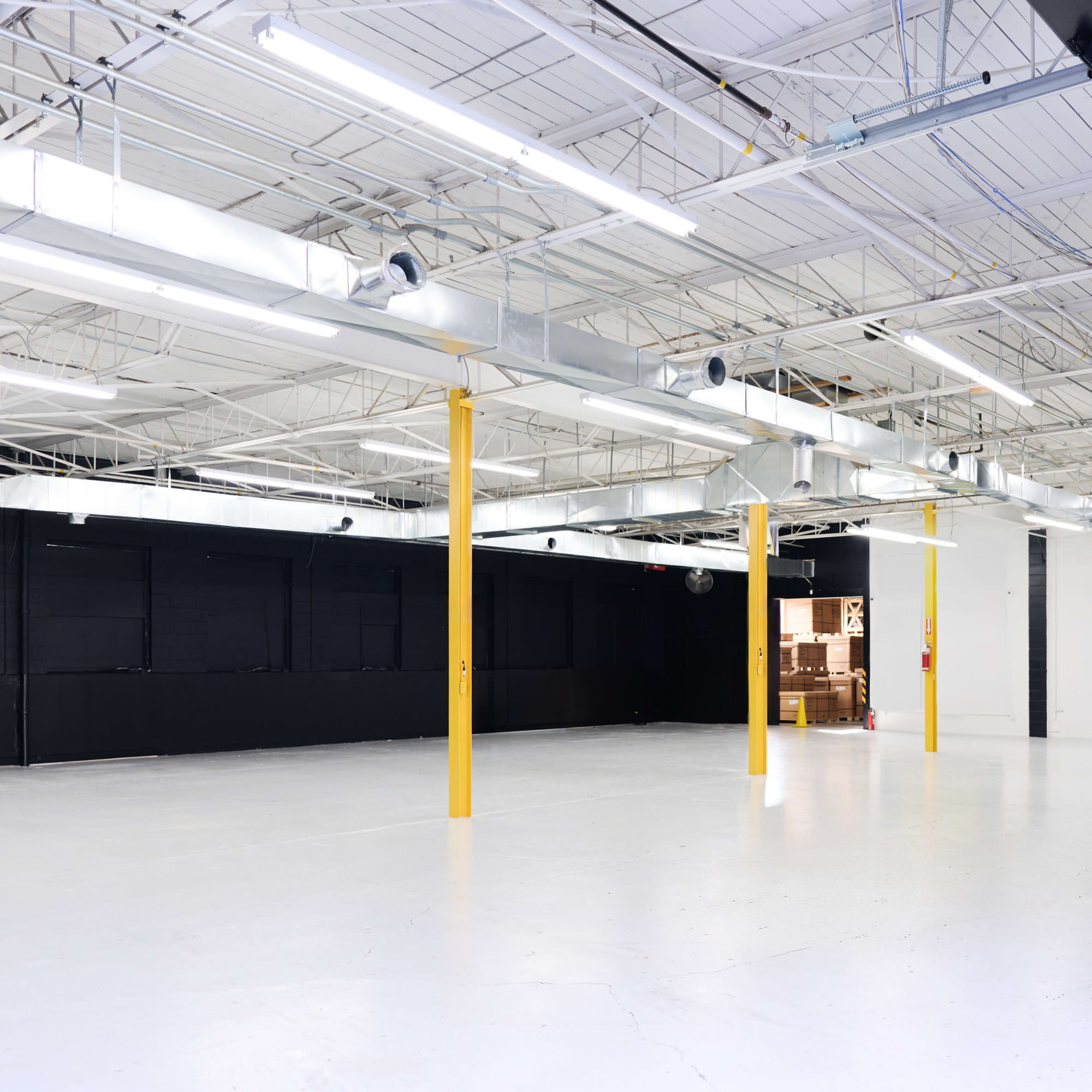 A spacious, empty industrial interior with white walls, polished concrete floors, and yellow support columns.