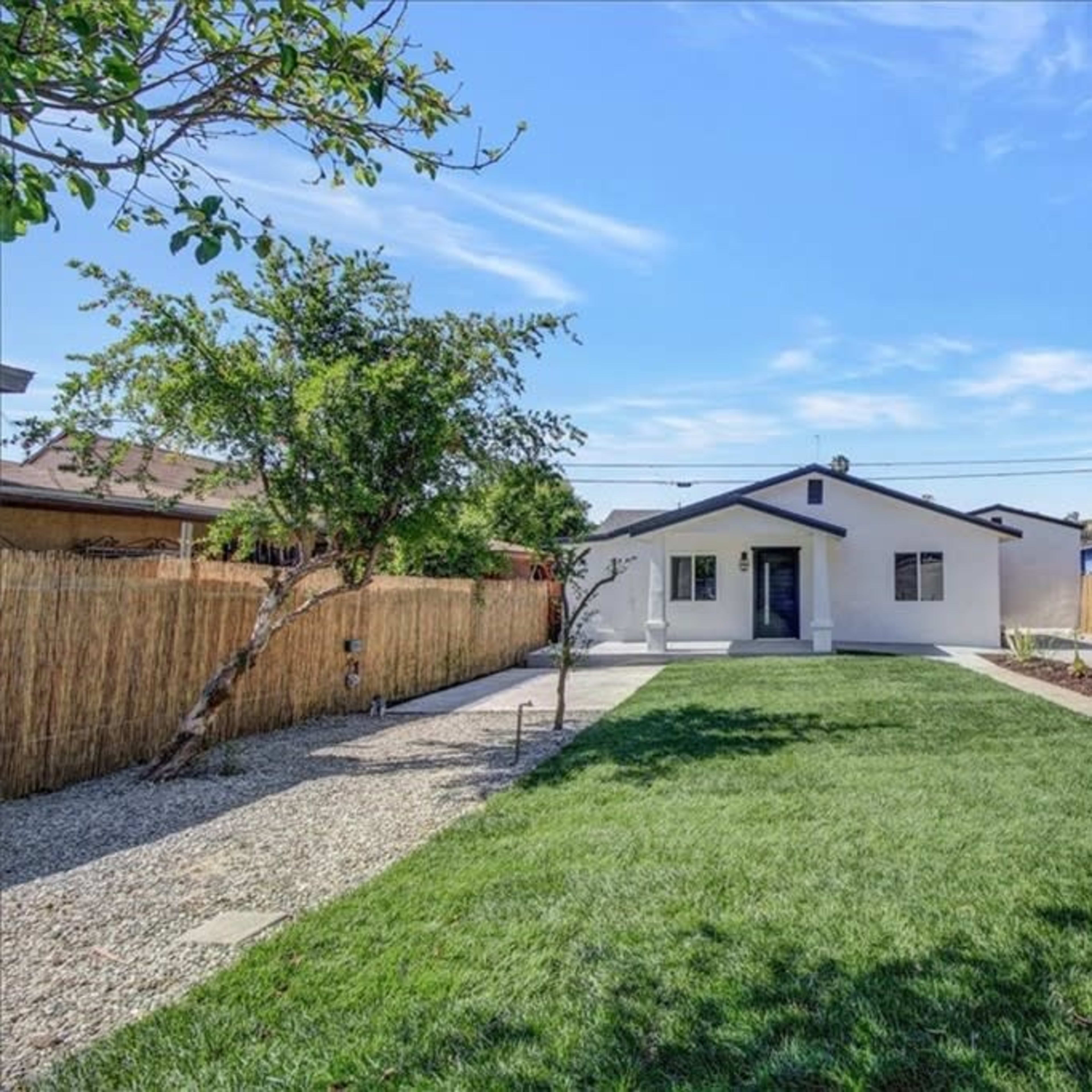 A single-story house with a front lawn and a gravel path, surrounded by bamboo fencing and landscaped areas.