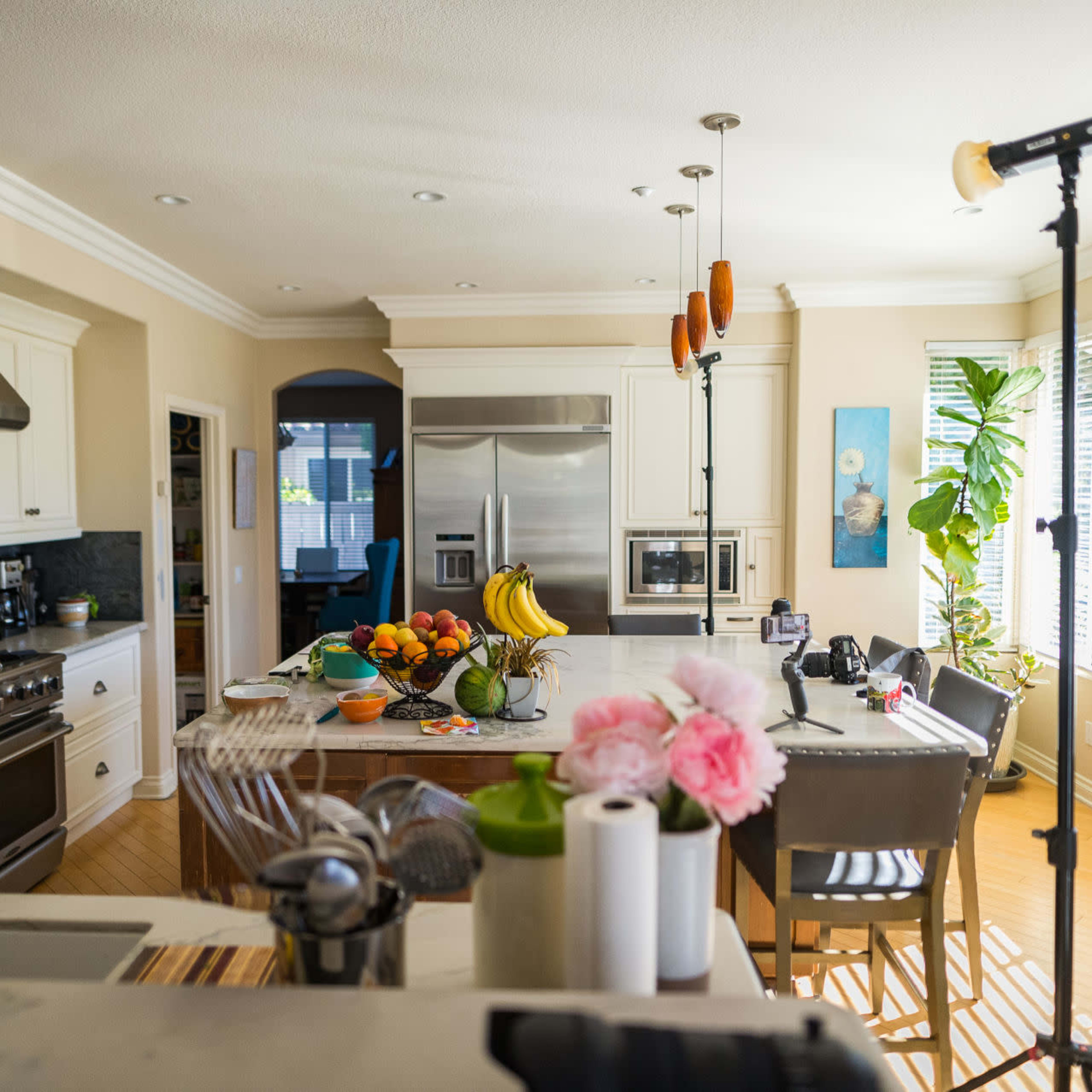 A well-lit kitchen features stainless steel appliances, a large island with fresh fruit, and a counter adorned with flowers and kitchen utensils.