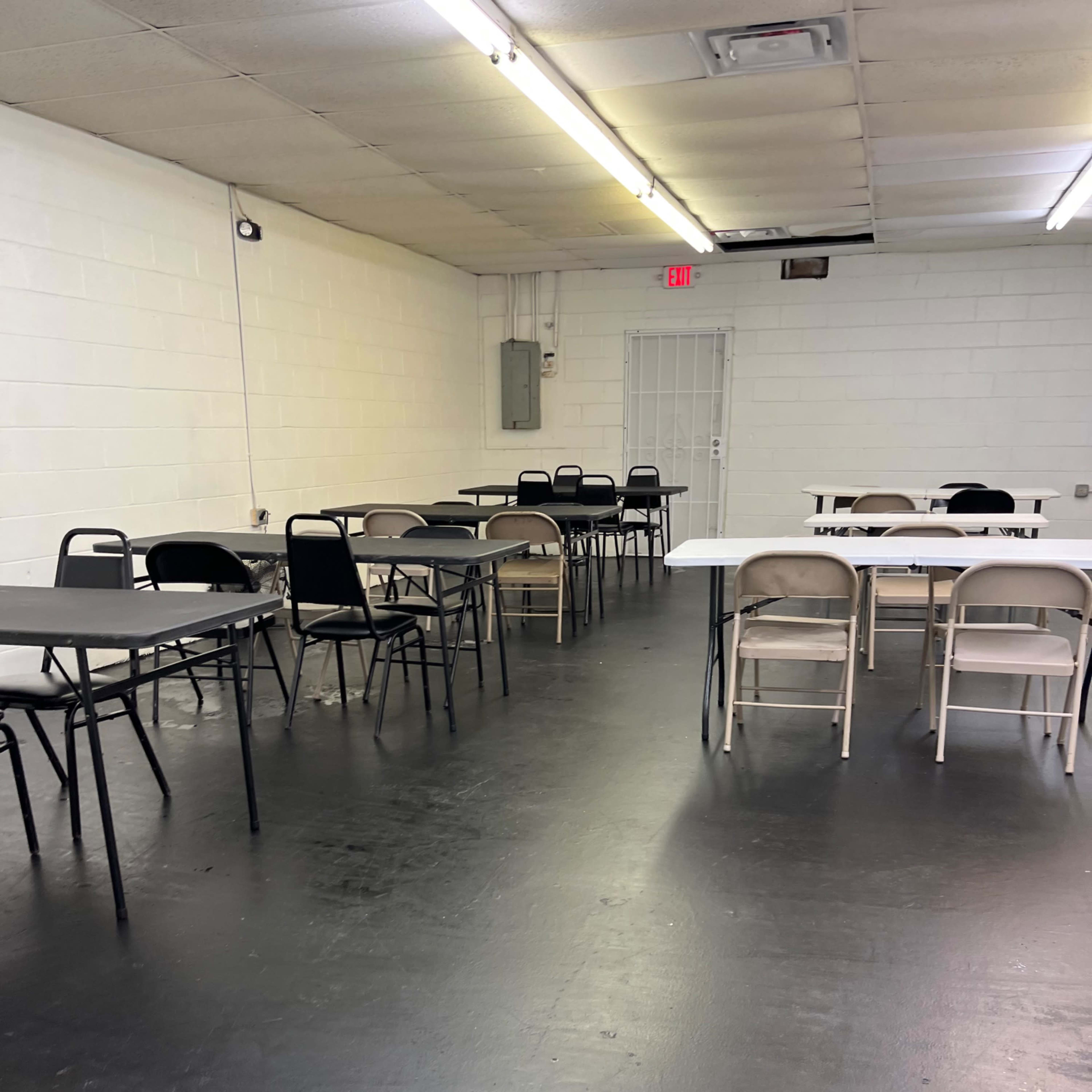 A spacious, empty room with several tables and chairs arranged around the space.