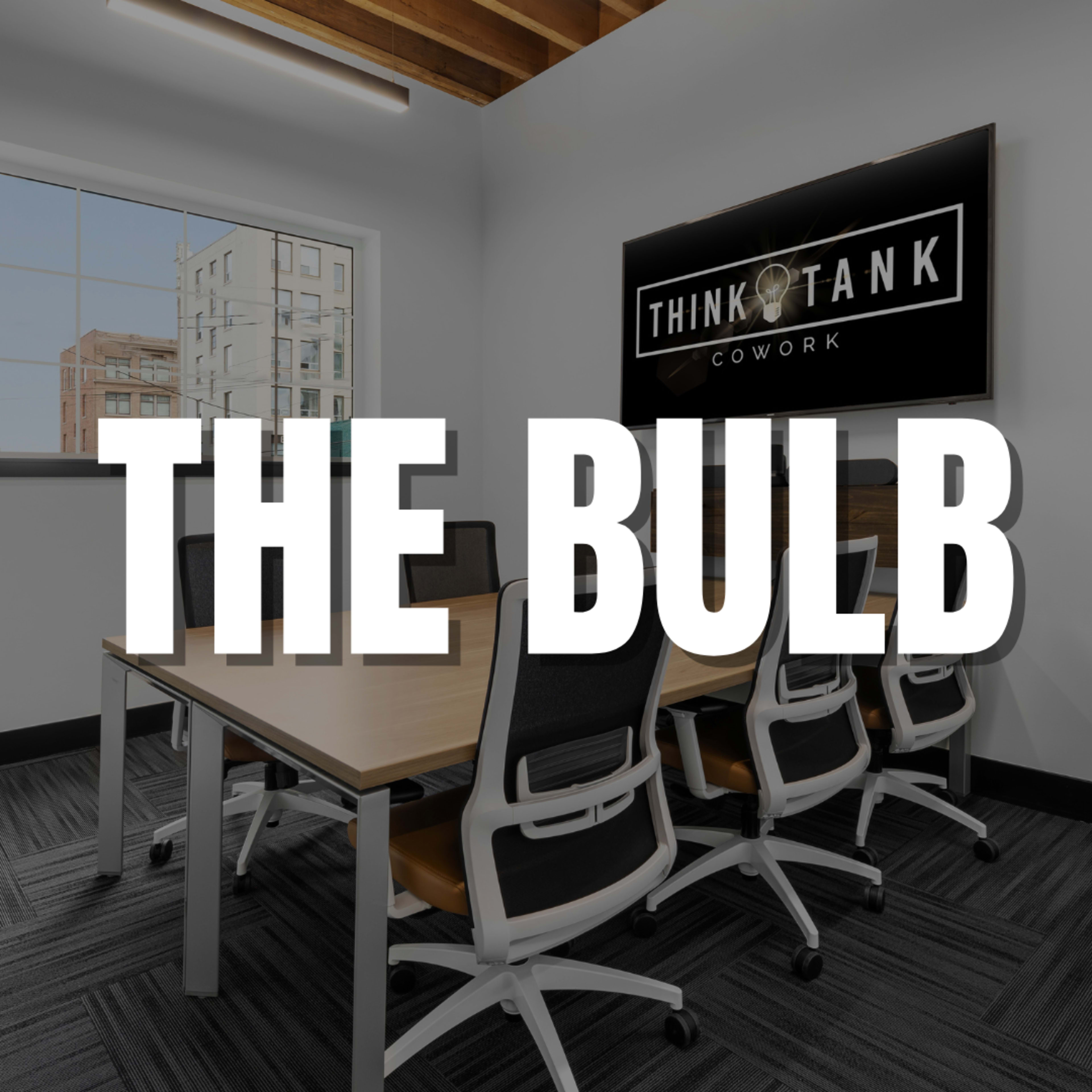 A contemporary conference room in a coworking space with a large window and a table surrounded by several chairs.
