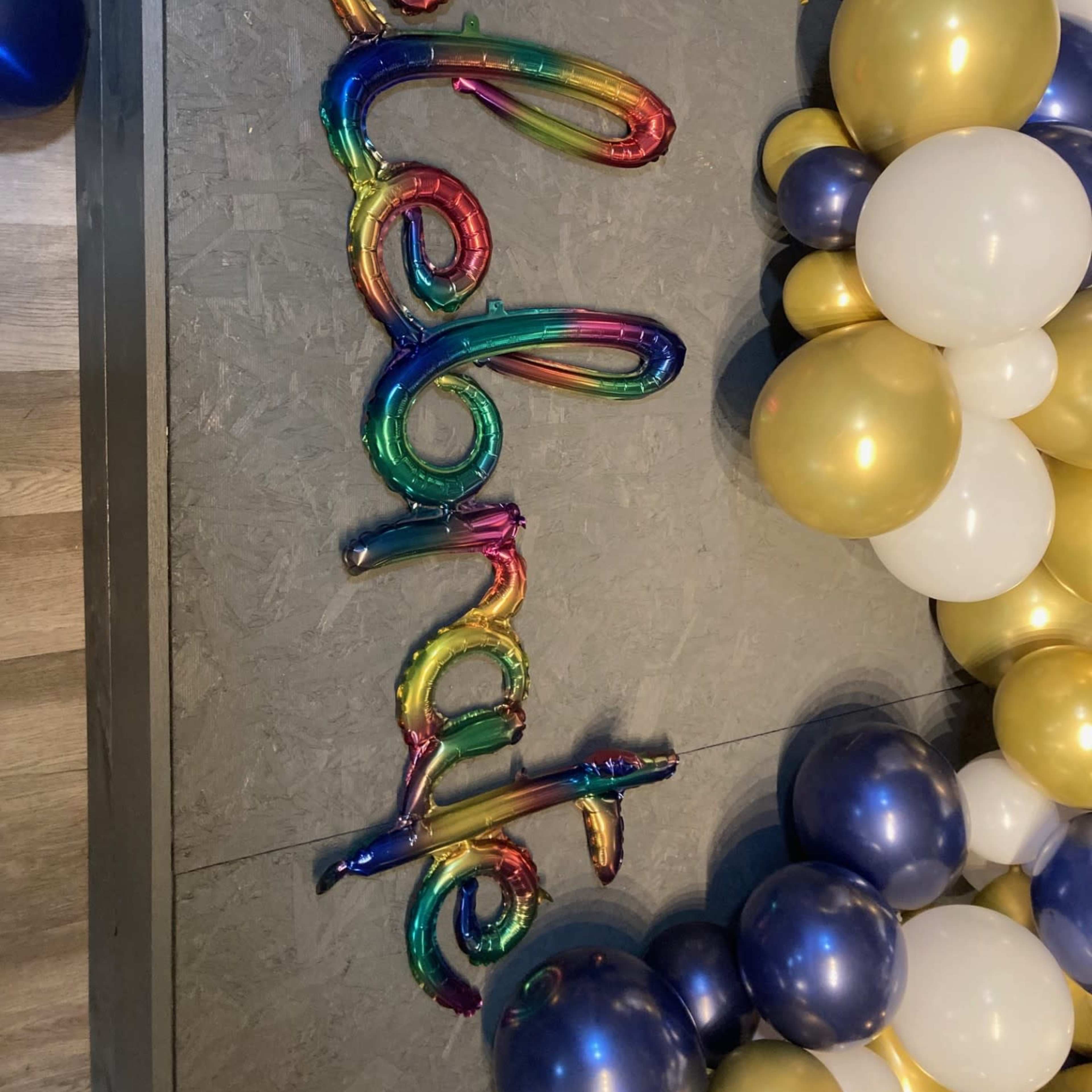 A colorful balloon decoration spelling out "celebrate" on a grey surface surrounded by assorted balloons.