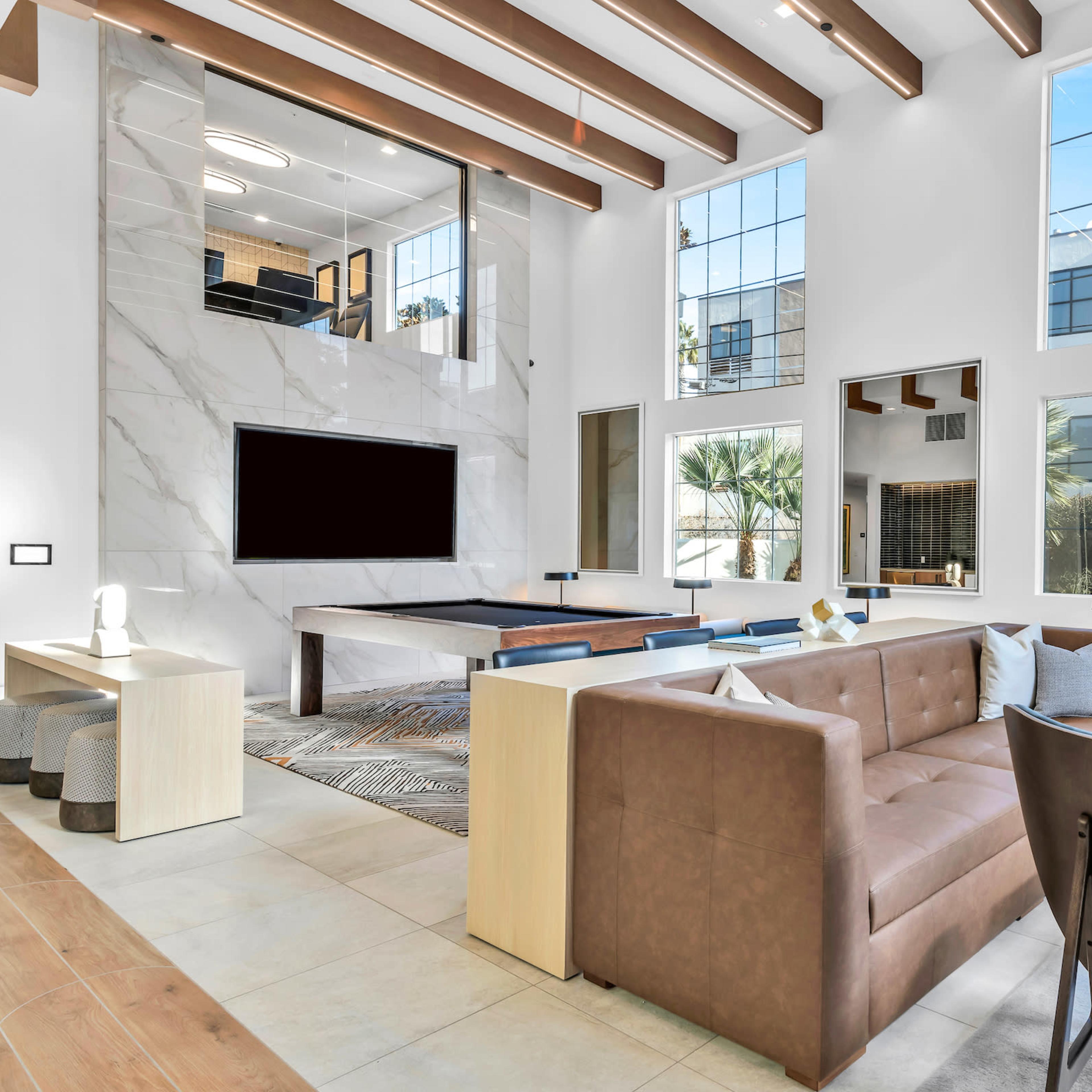 The spacious living room features large windows, a marble accent wall with a television, and modern furniture arranged around a coffee table.