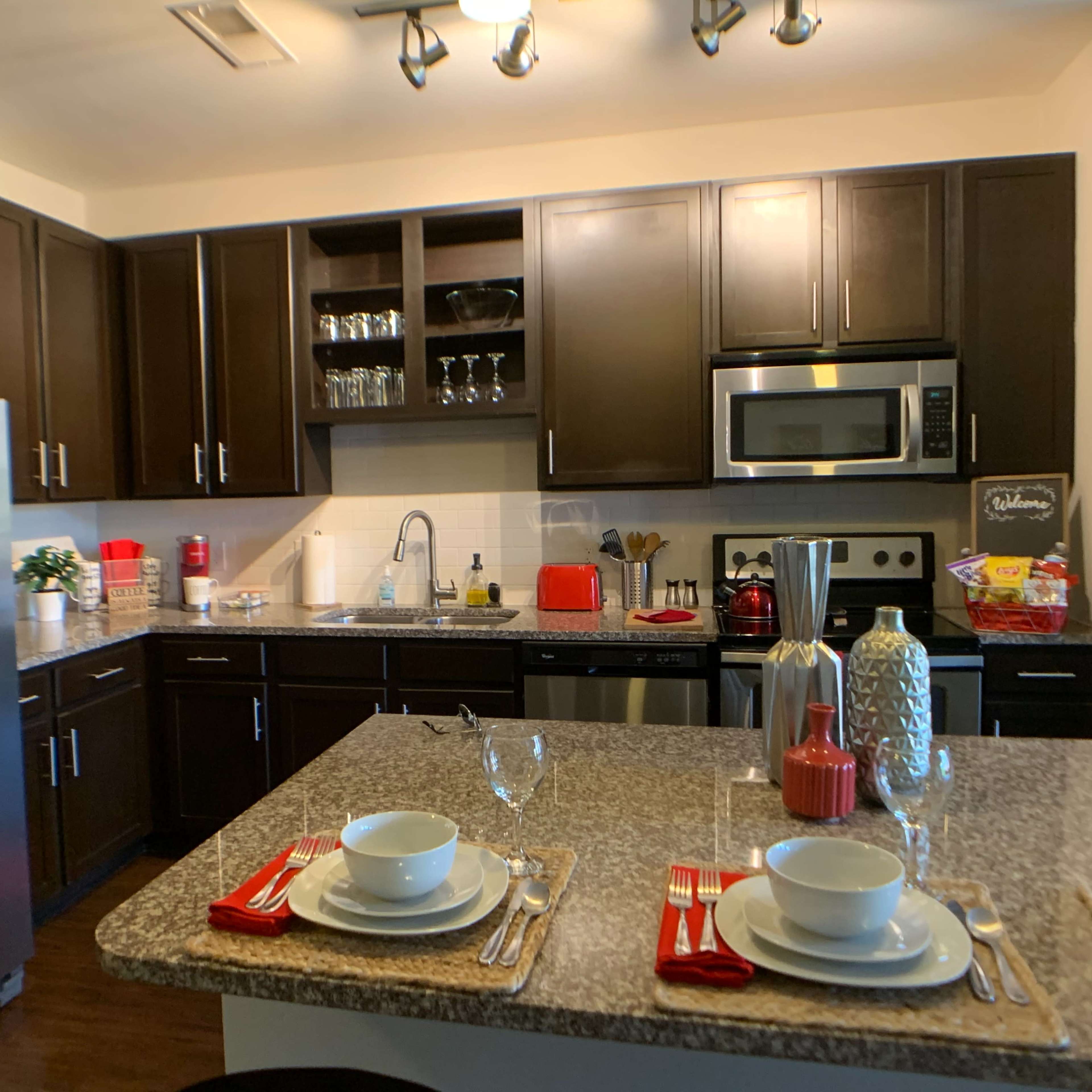 A modern kitchen with dark cabinetry, a stainless steel refrigerator, and a countertop set for two with plates and wine glasses.