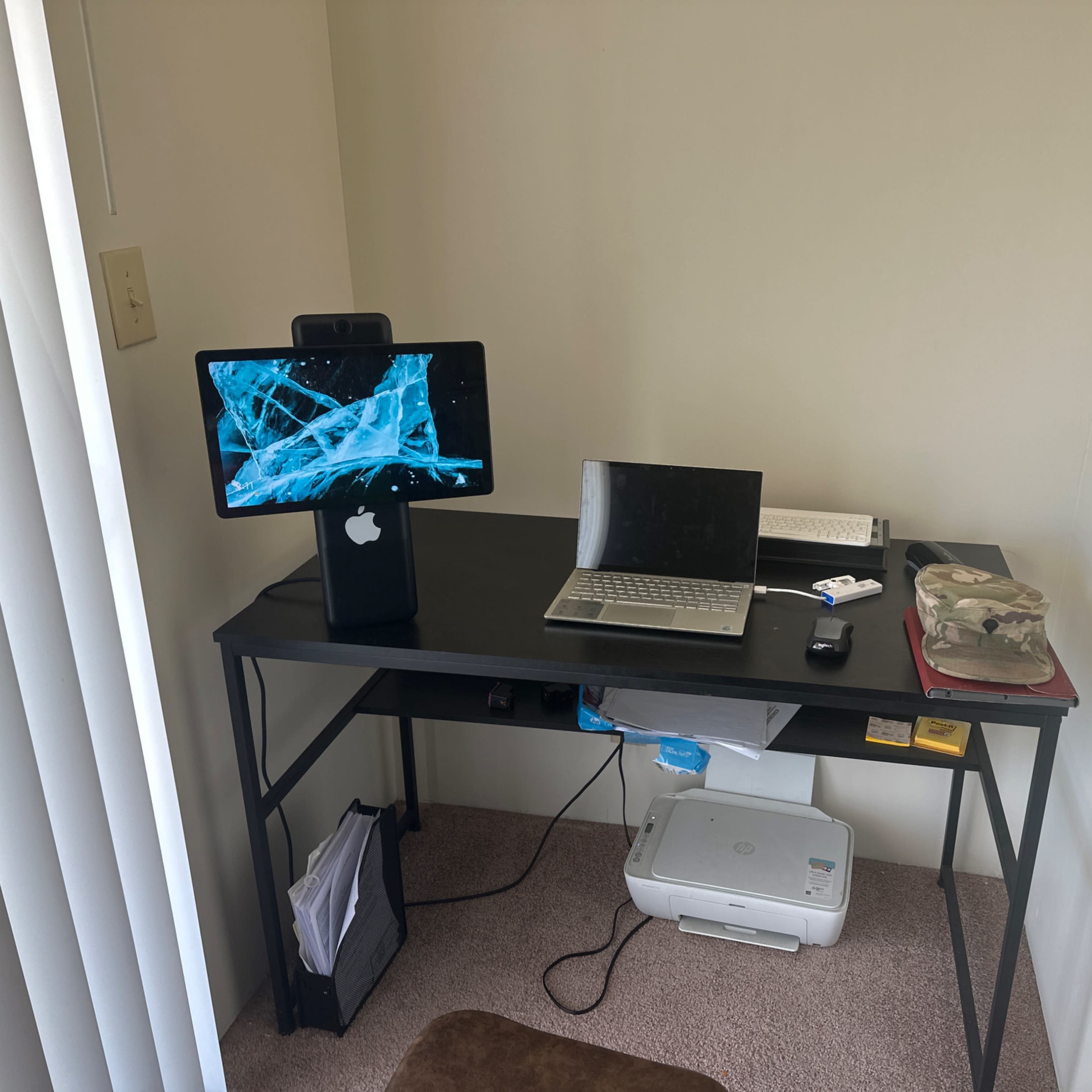 A compact desk setup in a corner with a desktop monitor, a laptop, a printer, and a few office supplies.