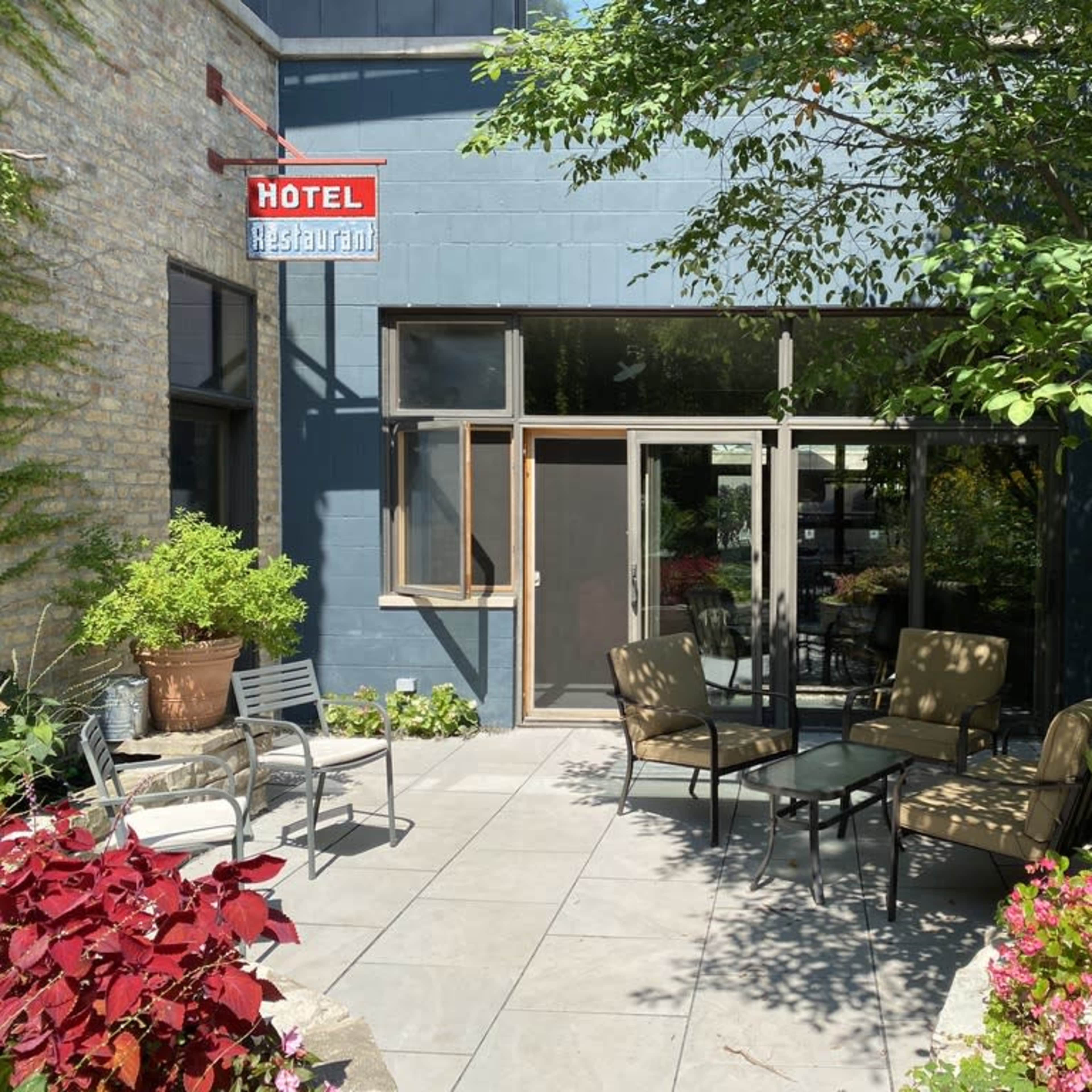 A patio area of a hotel restaurant featuring outdoor seating surrounded by plants and flowers.