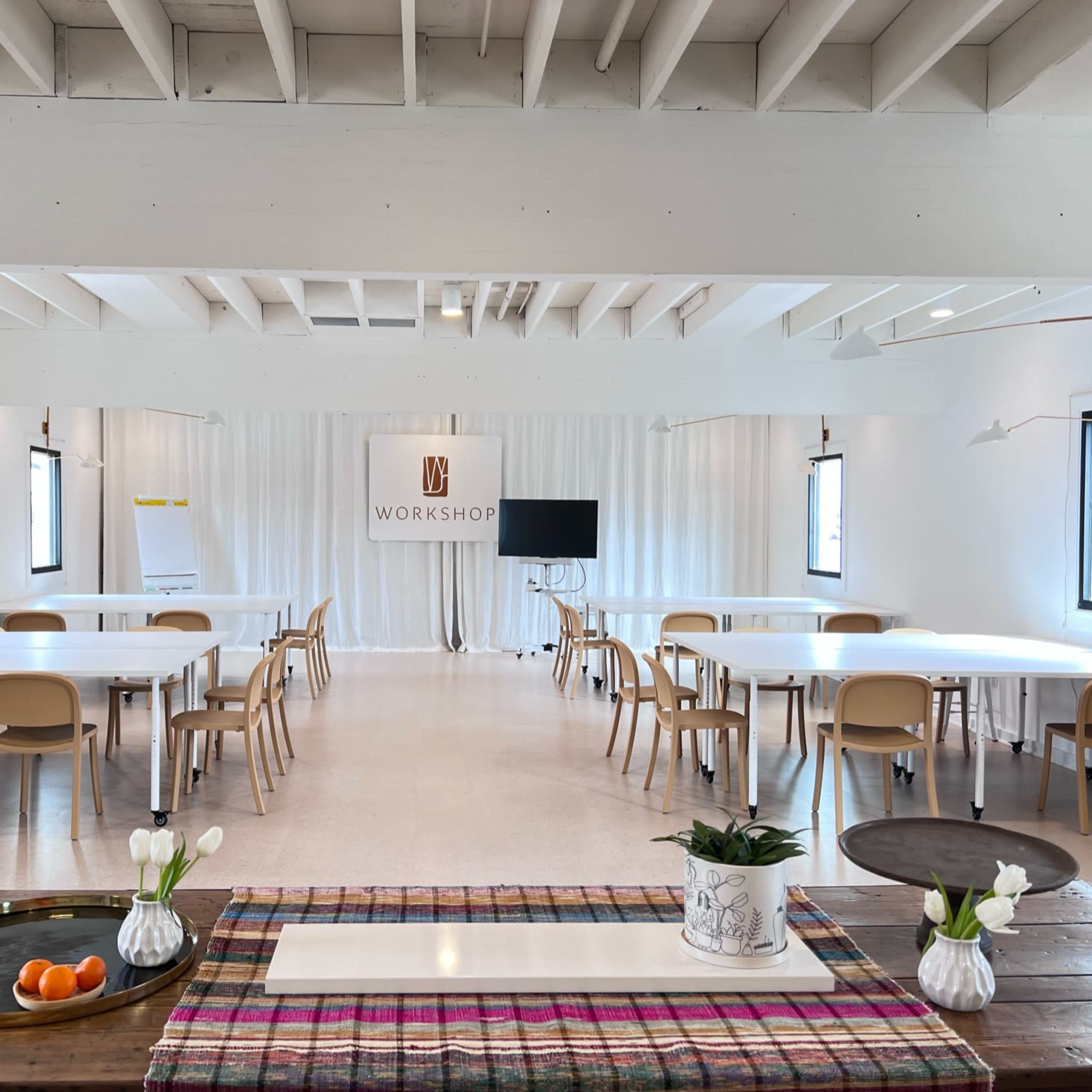 A bright, modern workshop space with several tables, chairs, and a screen at the front, all arranged in a clean, organized manner.