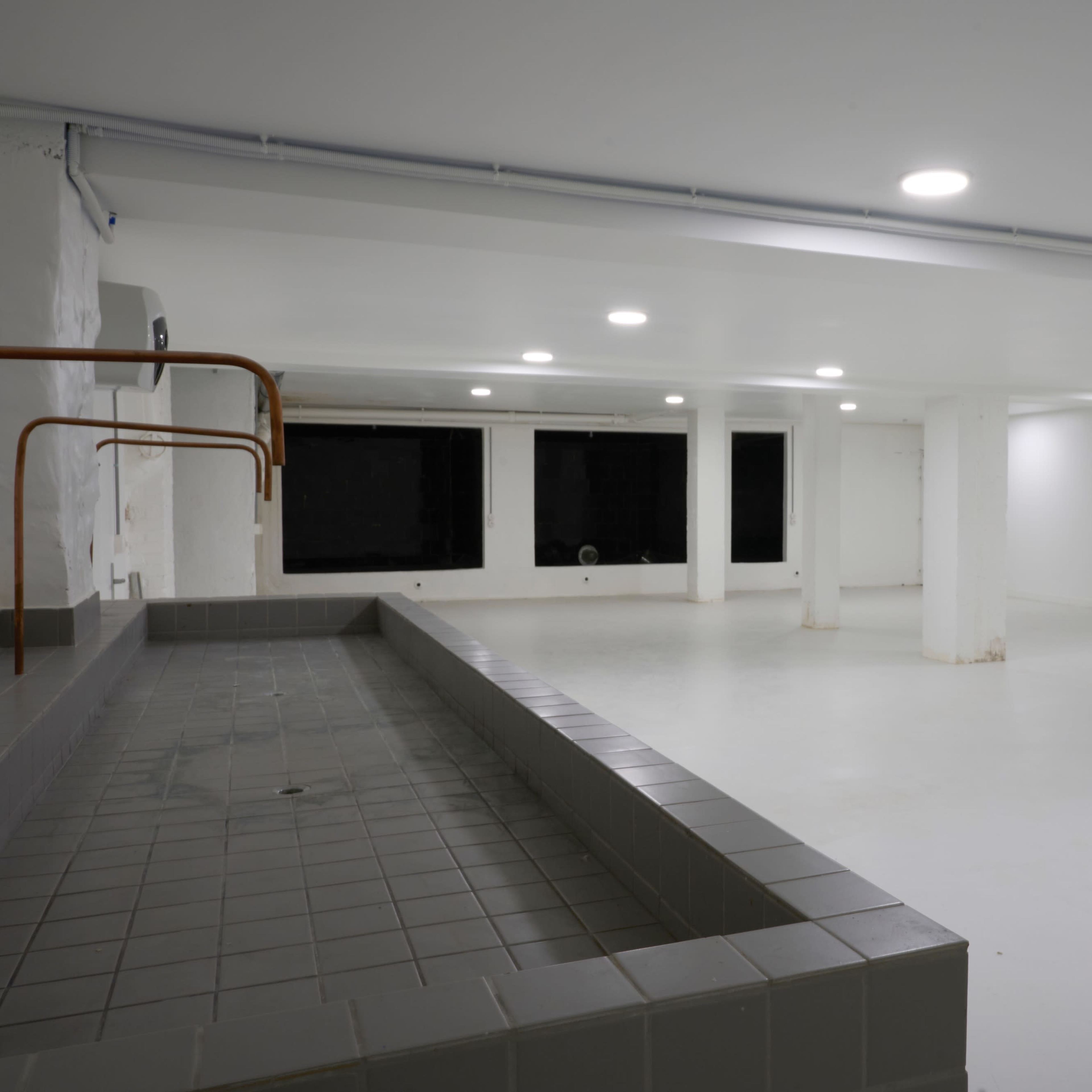 An empty, well-lit indoor space with a tiled area and a long, low basin along one wall.