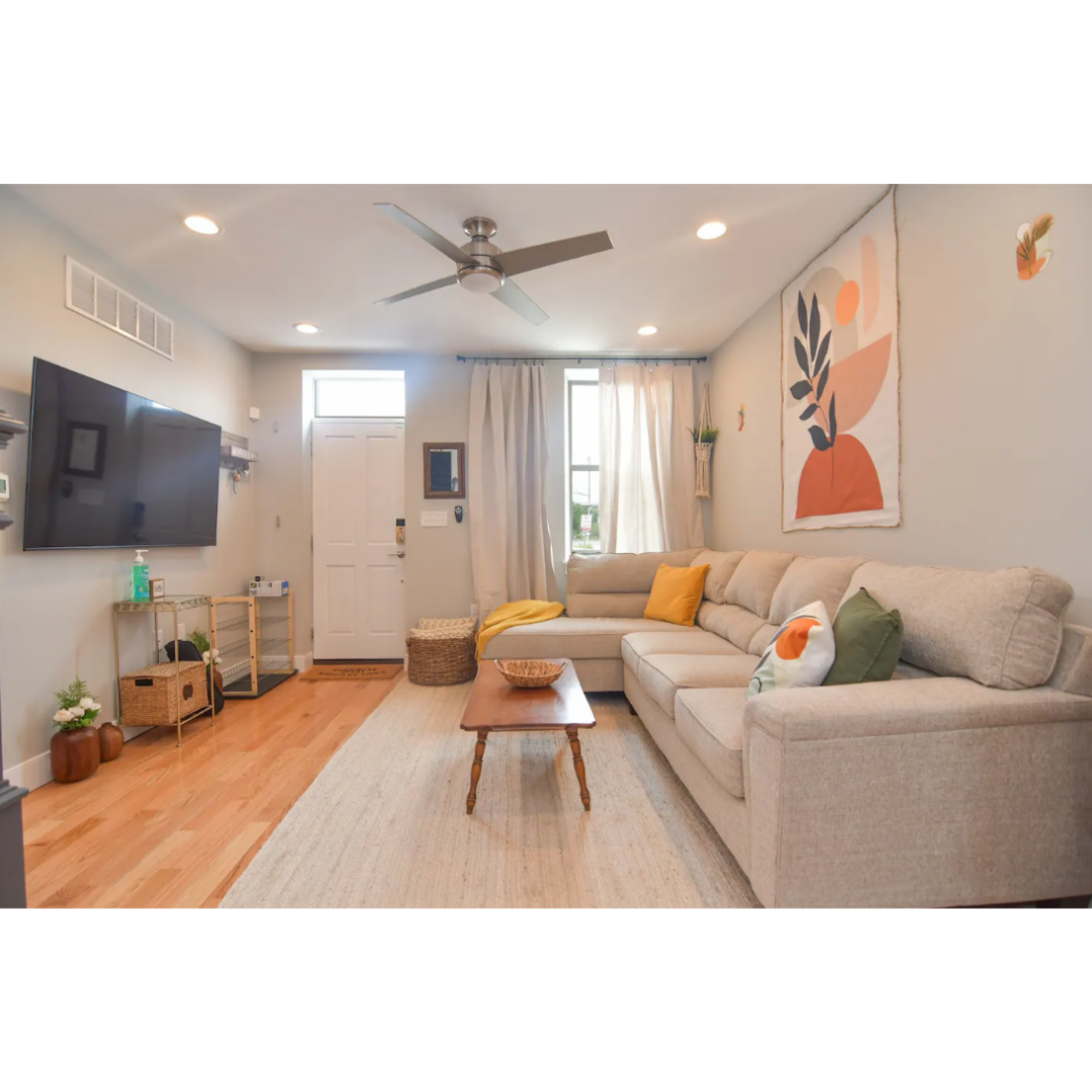 A modern living room features a light-colored sofa, a wooden coffee table, and wall decorations, with a door and windows allowing natural light.