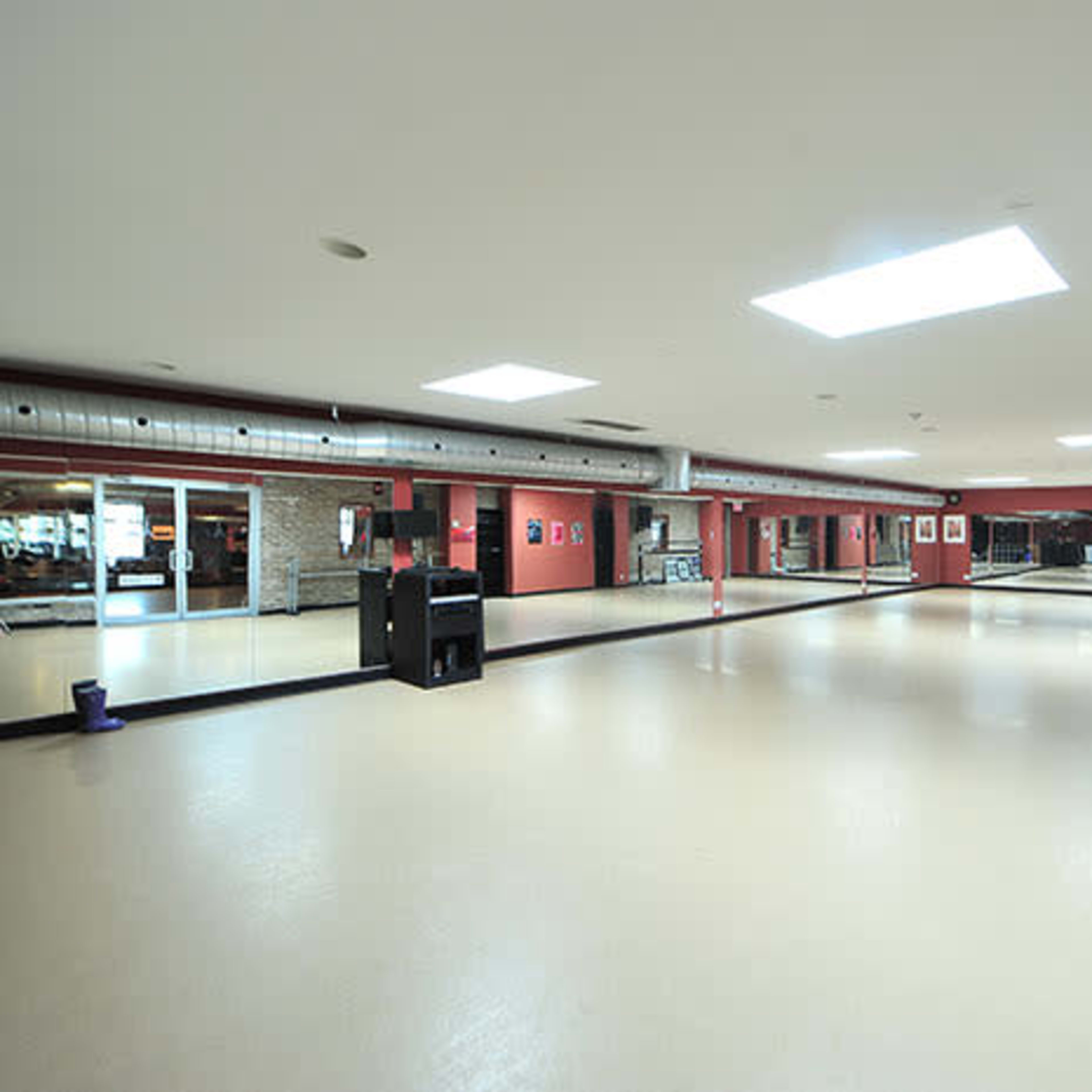 A spacious dance studio with large mirrors, a light-colored floor, and a skylight illuminating the area.