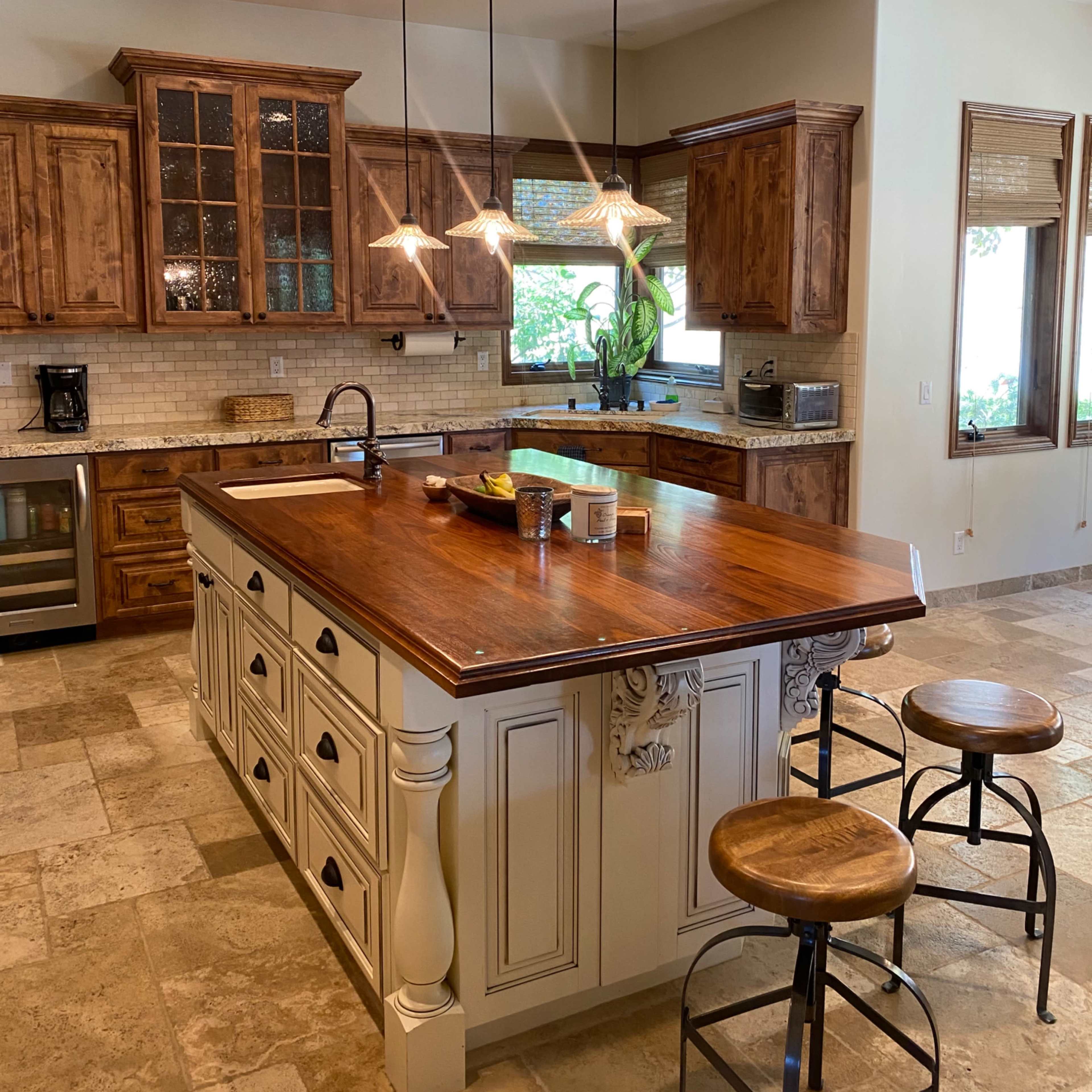 A spacious kitchen with wooden cabinetry, a large island with a dark wooden countertop, and metal bar stools.