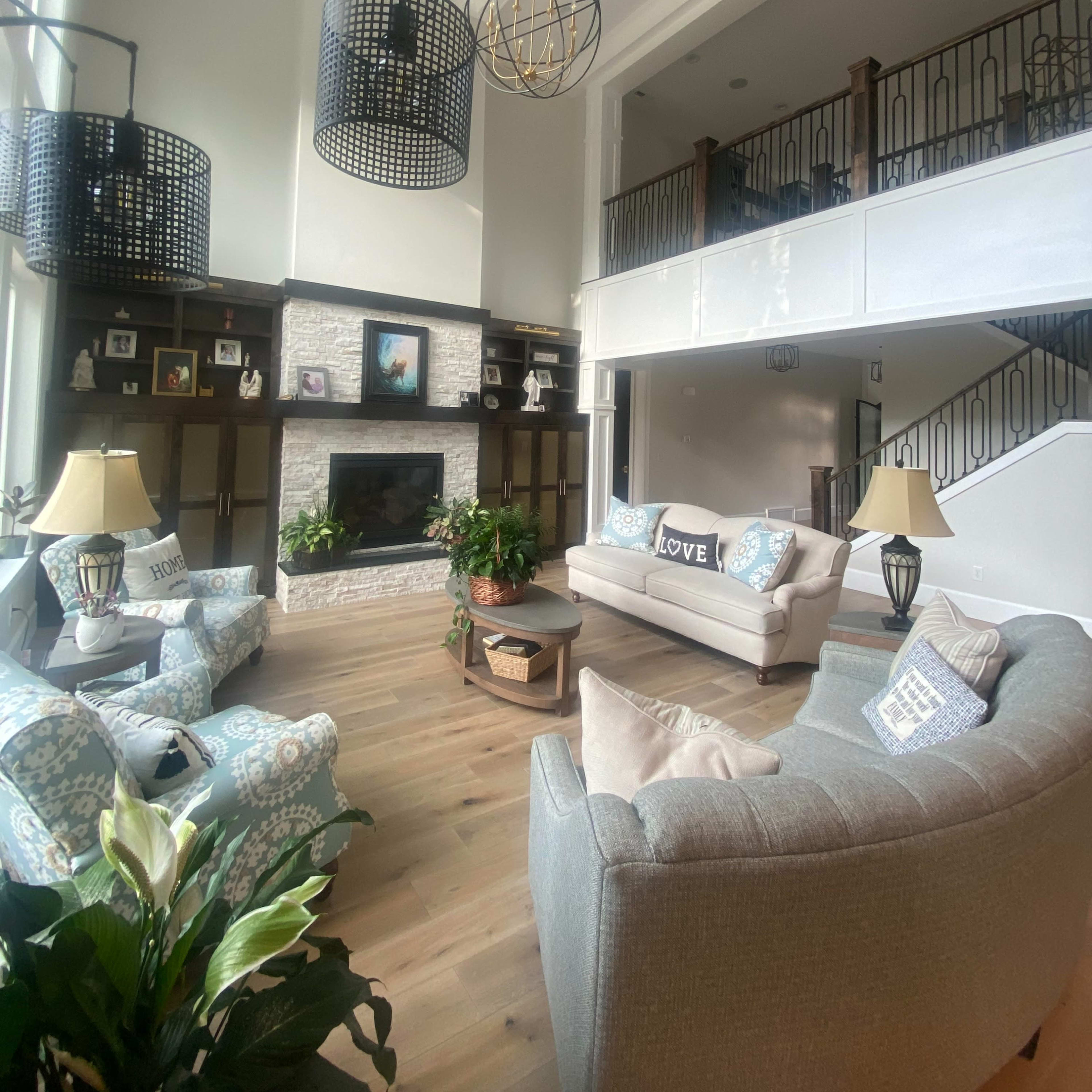 The living room features a high ceiling with large windows, a stone fireplace, and comfortable seating arranged around a coffee table.