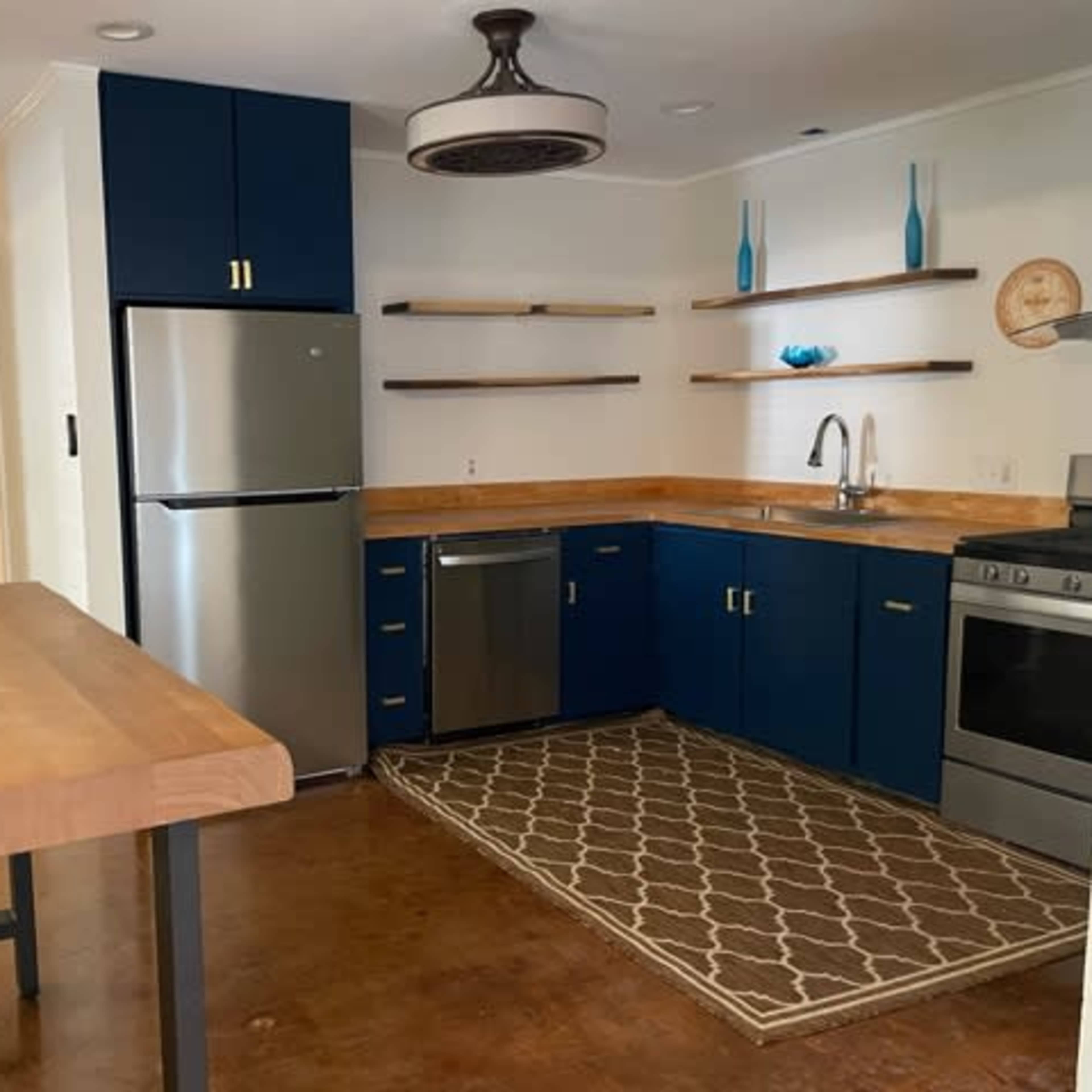 A modern kitchen featuring blue cabinets, stainless steel appliances, wooden countertops, and decorative shelves against a beige wall.