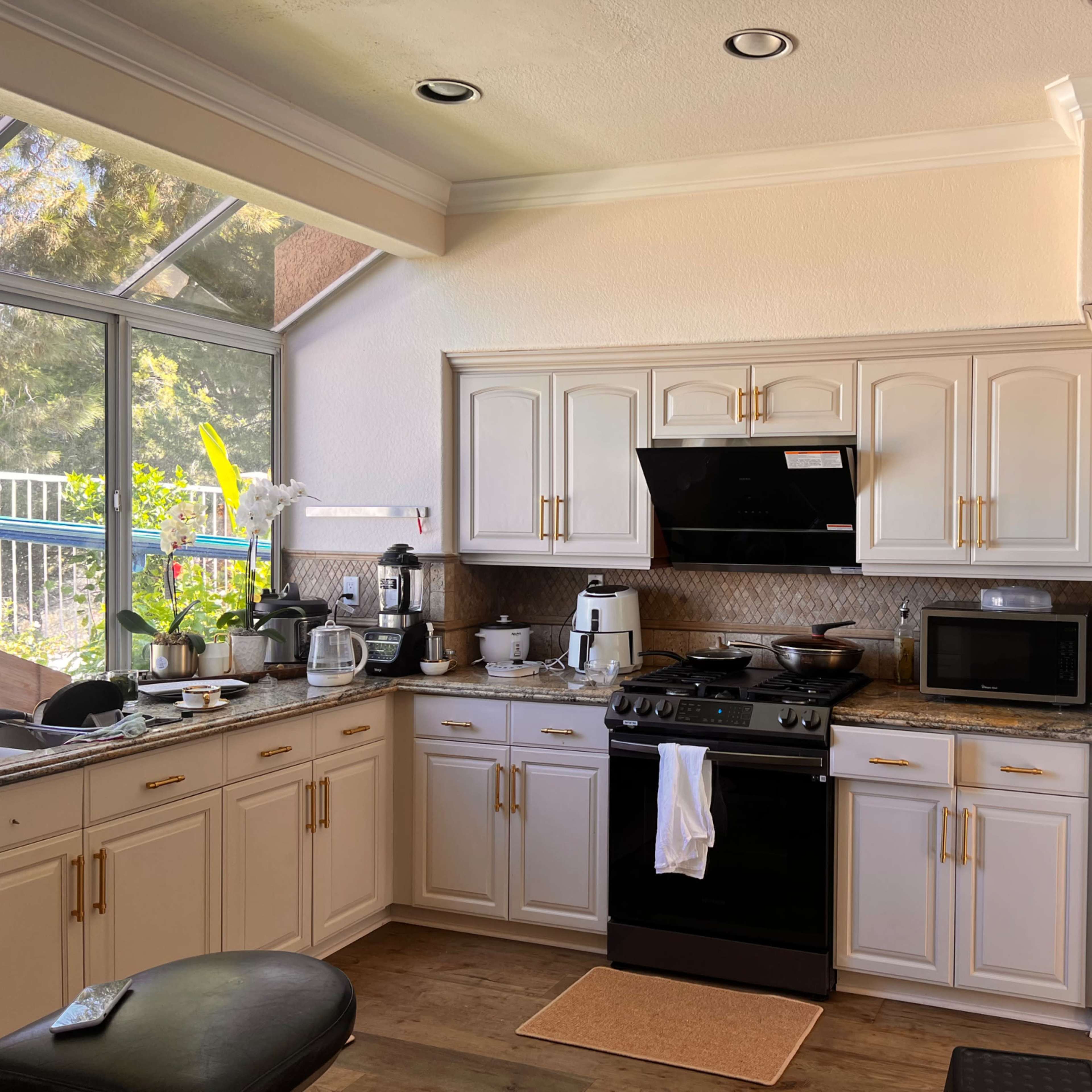 A modern kitchen with white cabinetry, a black stove, a microwave, and various kitchen appliances arranged along the countertop.