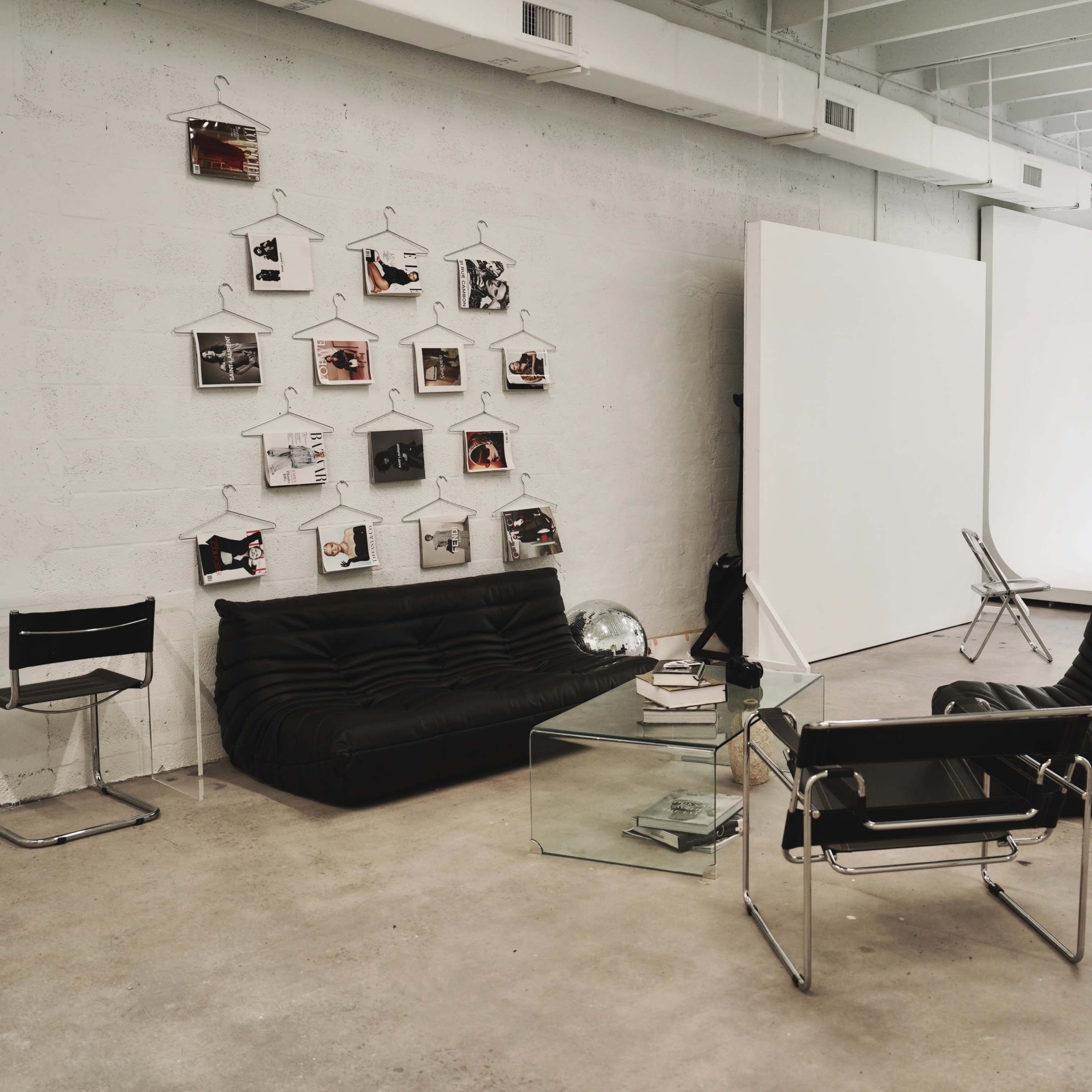 A modern studio space features black sofas, a glass table, and a photo display on the wall, with a large white backdrop for photography.