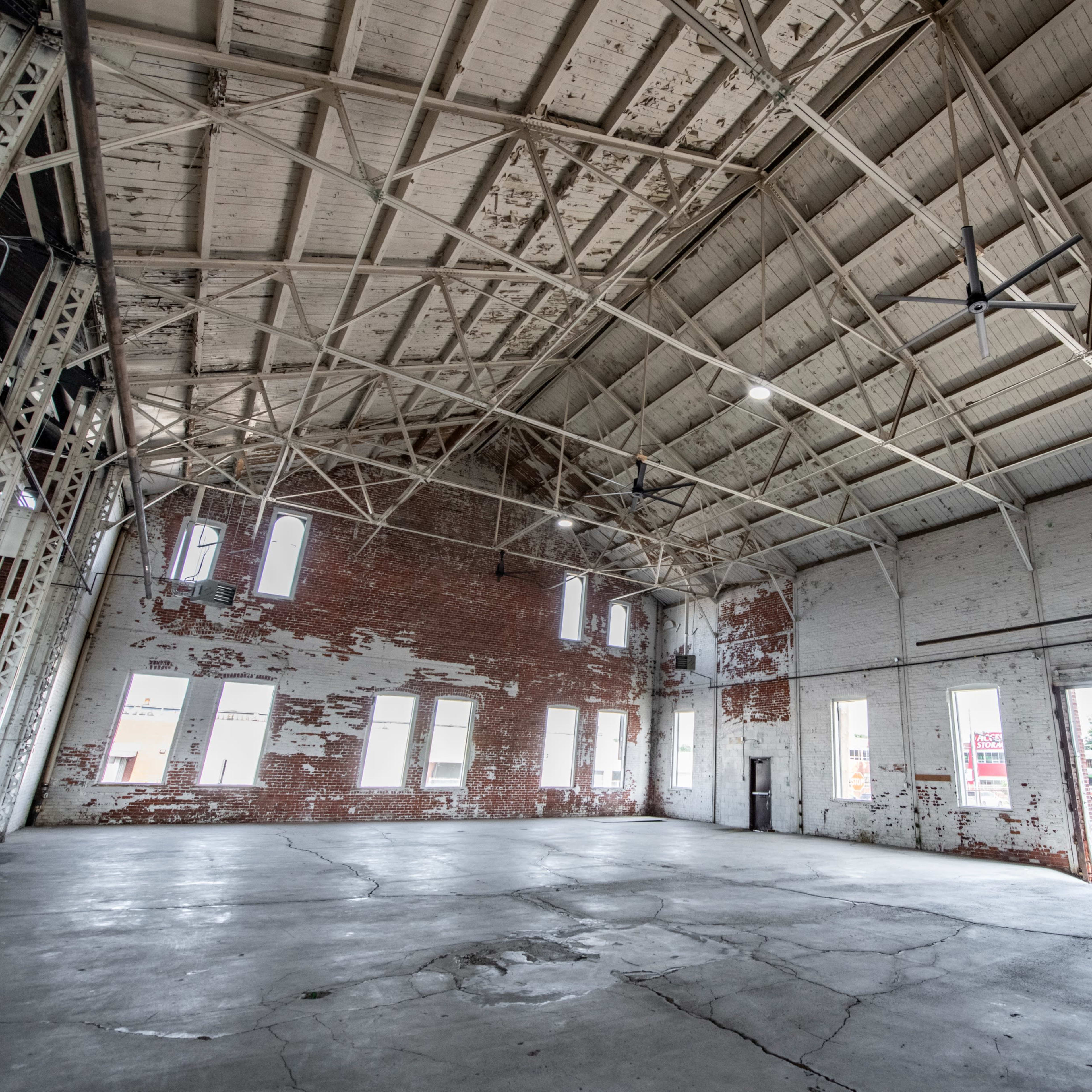 A large, empty warehouse with a high, metal-truss ceiling and exposed brick walls.