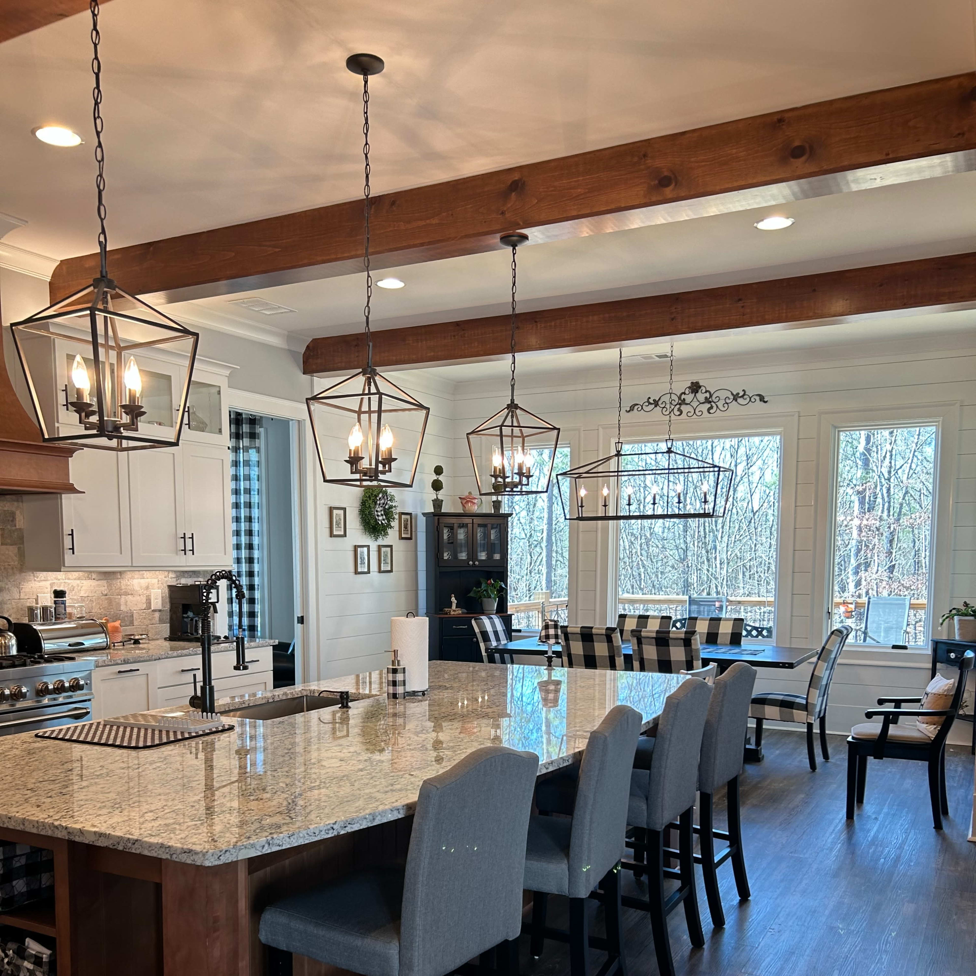 A modern kitchen featuring a large island with bar stools, pendant lighting, and a dining area with a window view.
