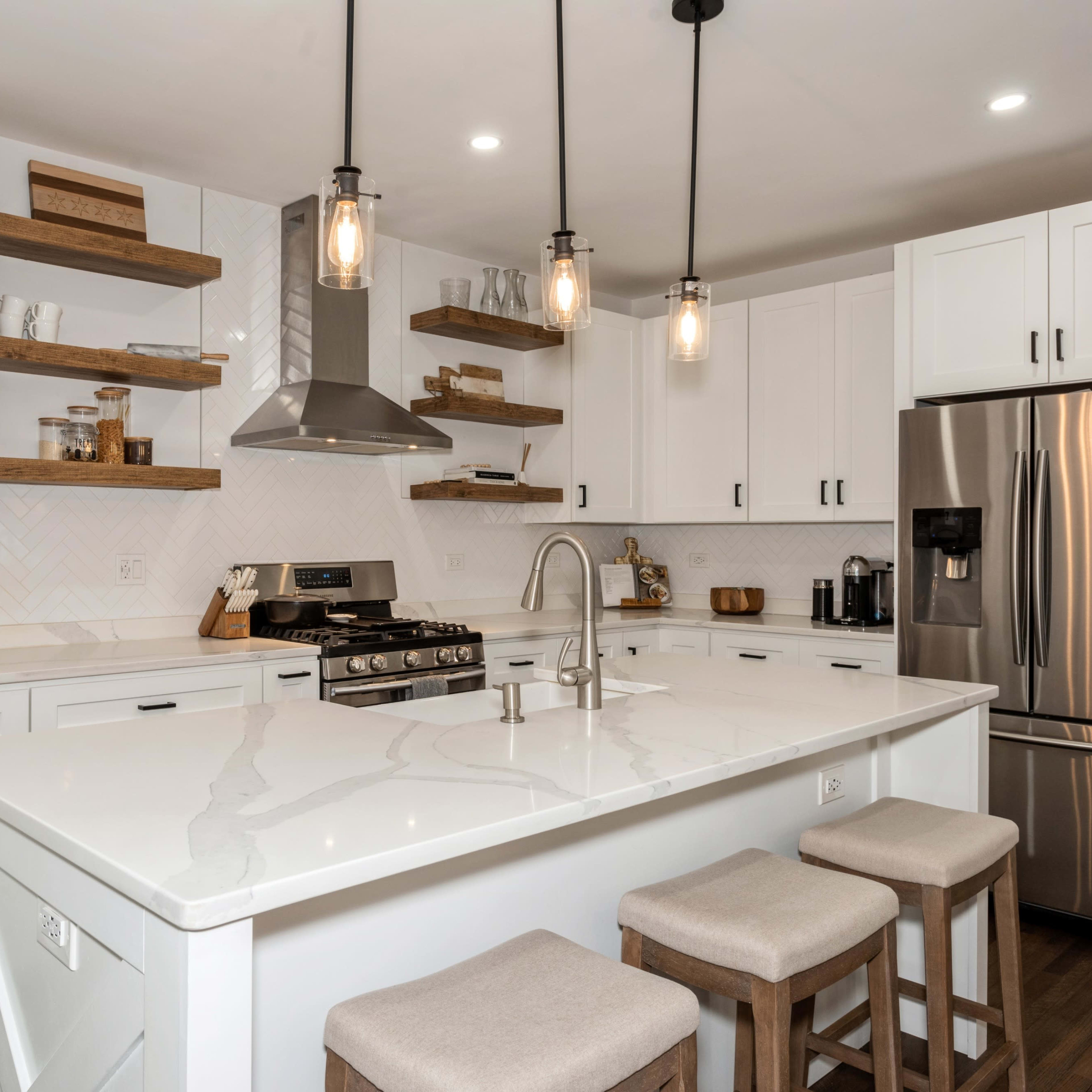 A modern kitchen featuring white cabinetry, a large island with seating, and open shelves displaying kitchenware.