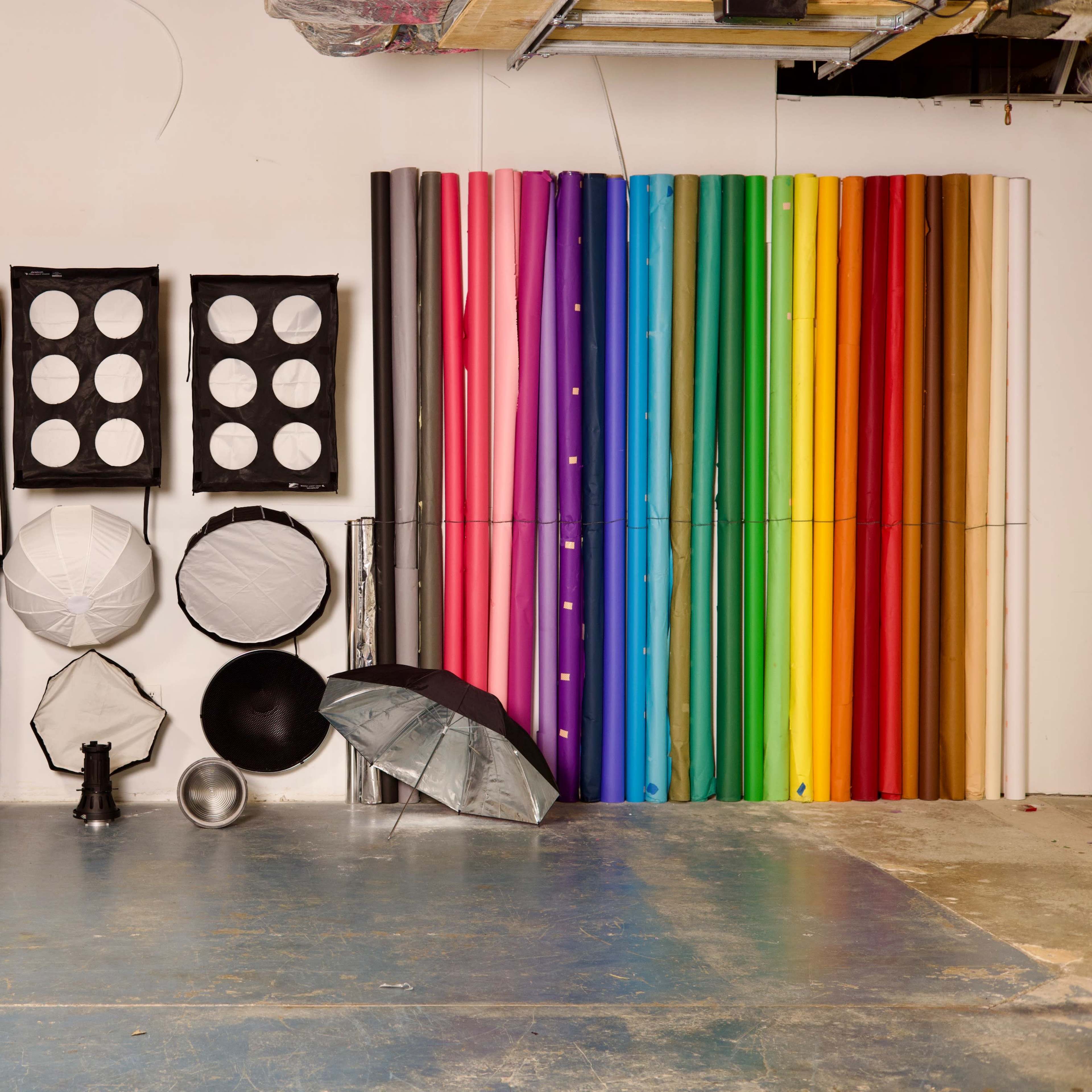 A variety of photography equipment arranged on a wall, including light modifiers, backdrops, and umbrellas.
