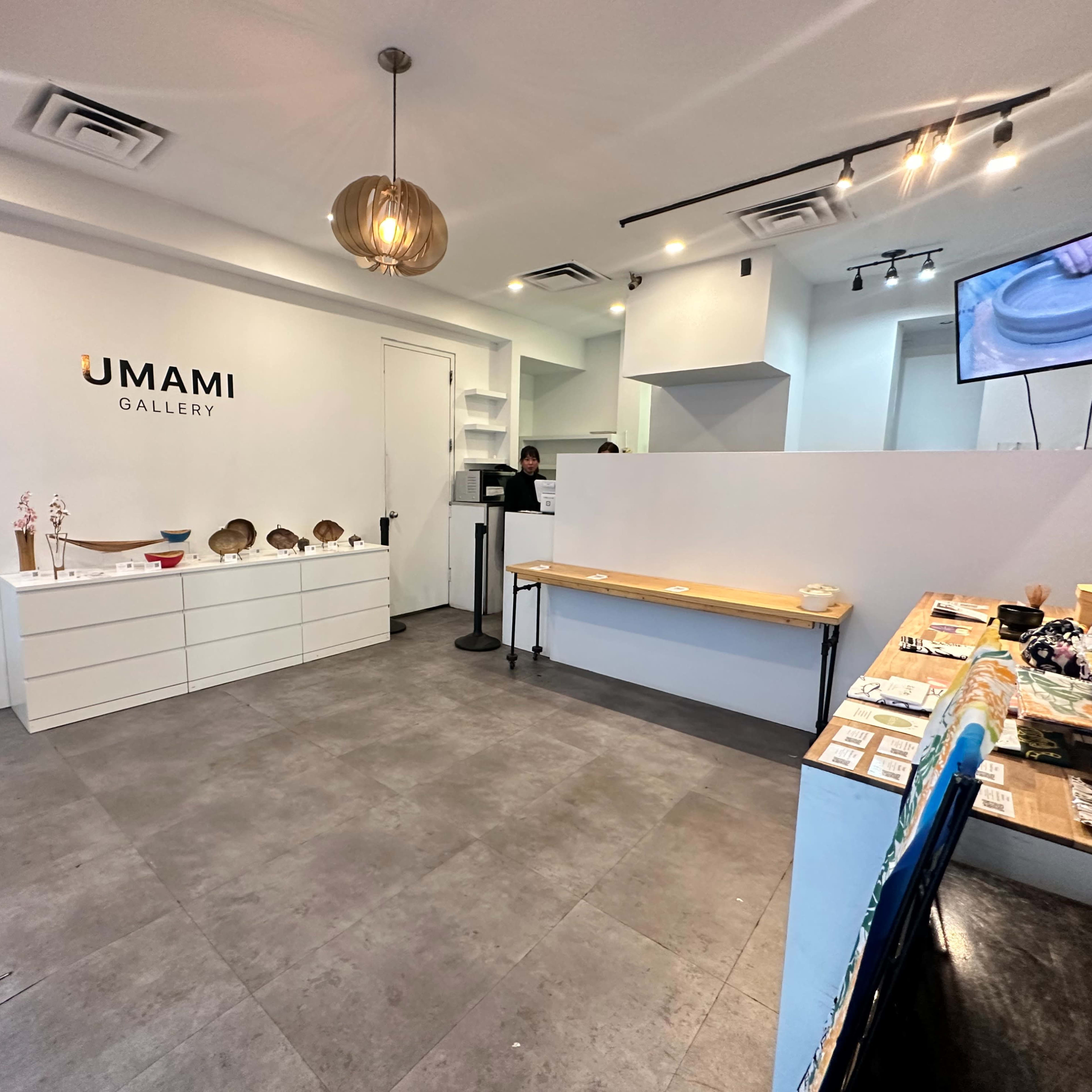 A modern gallery space featuring a reception area, display shelves, and various art items on a table.