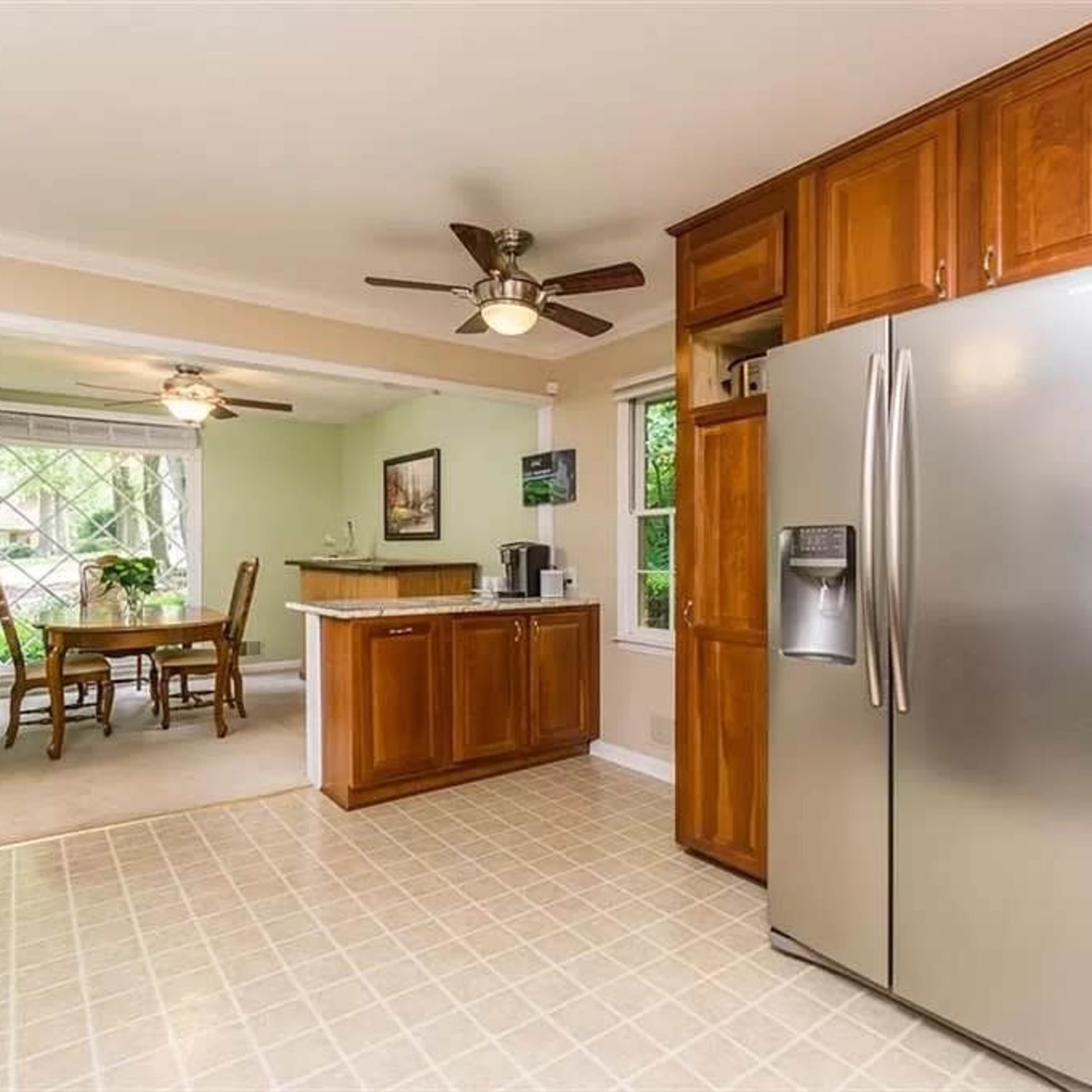 A kitchen with wooden cabinets, a stainless steel refrigerator, and a view of a dining area through an open doorway.