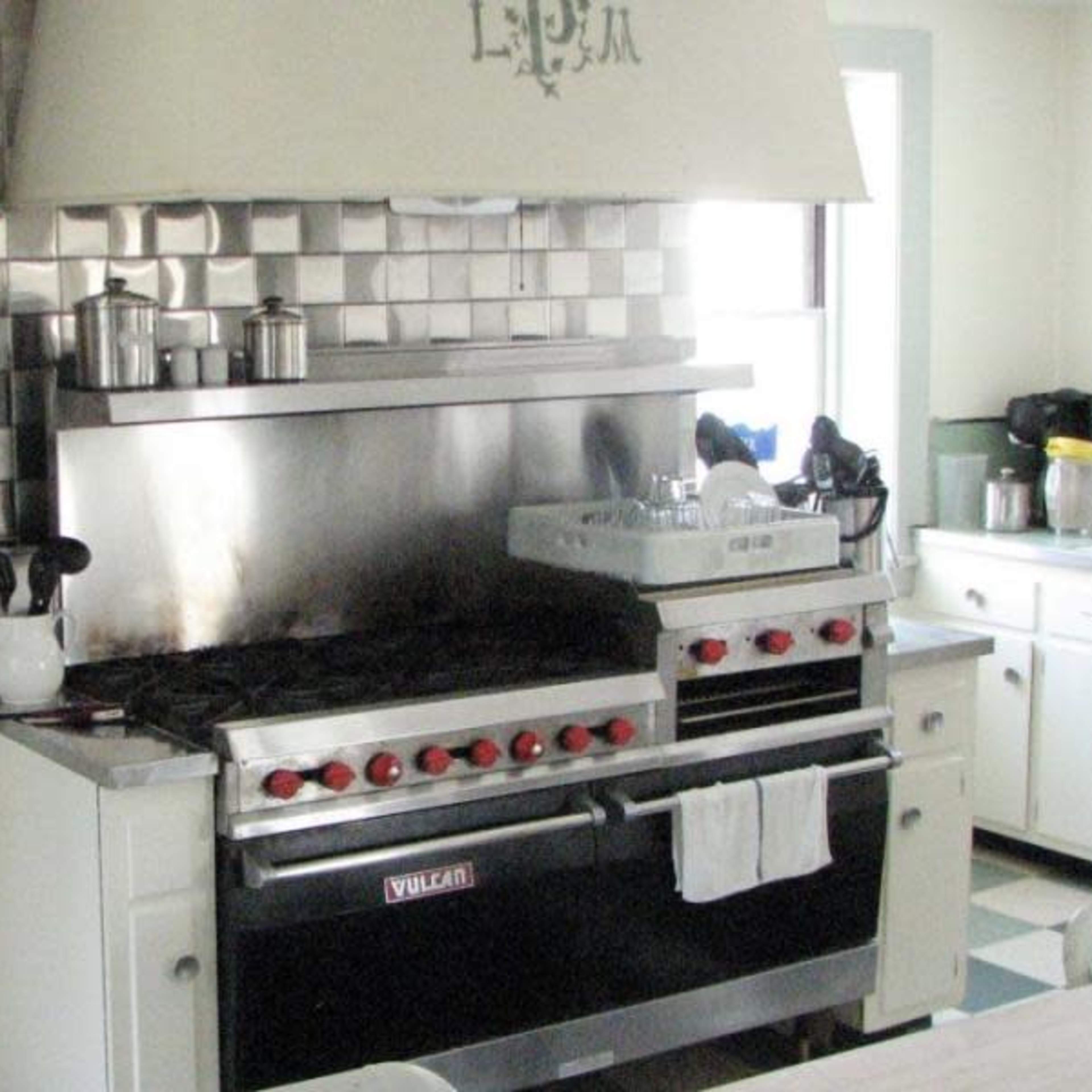 A kitchen with a stainless steel gas range, a hood above it, and various kitchen appliances on the counter.