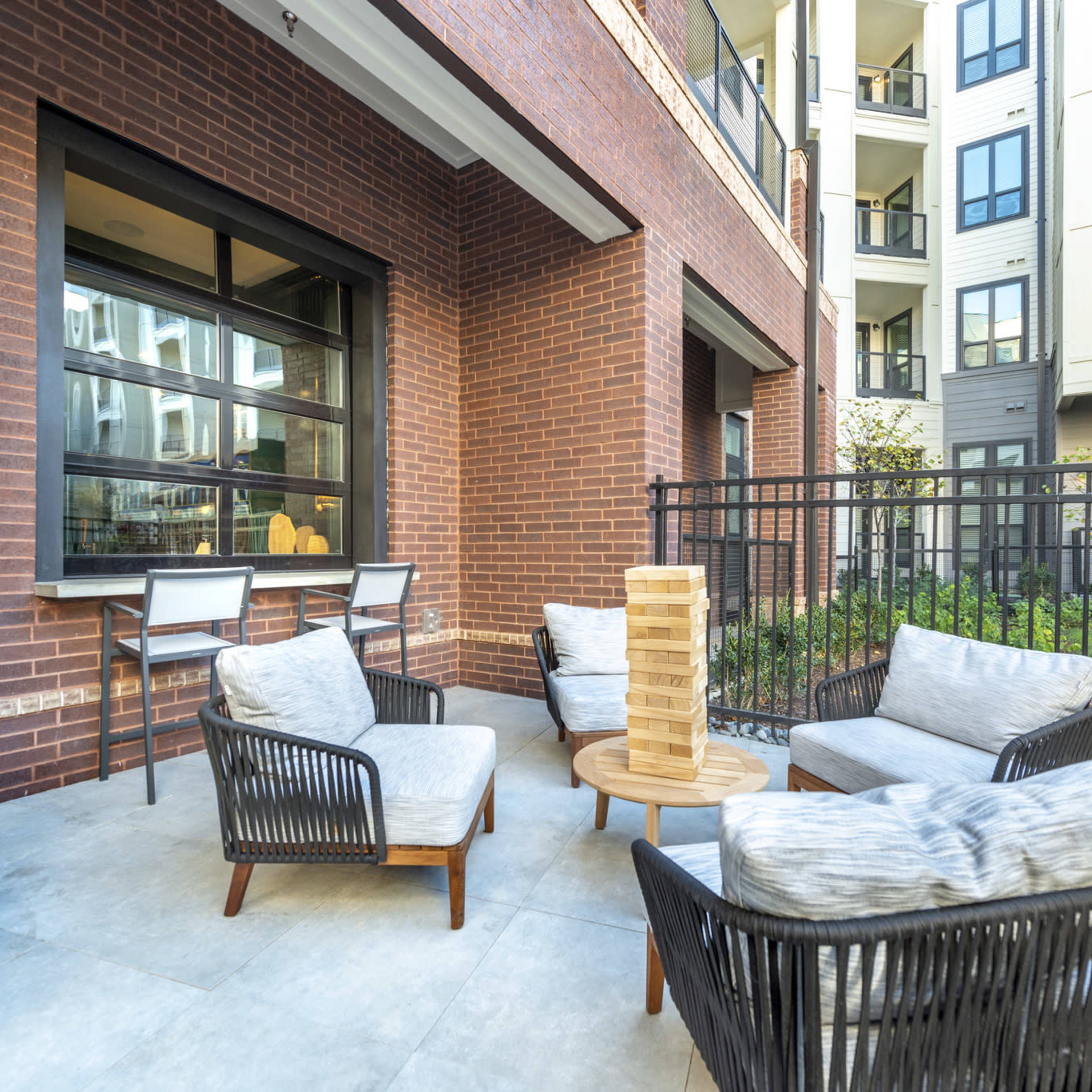 A modern outdoor seating area with four chairs and a small table surrounded by brick walls and a garden space in the background.