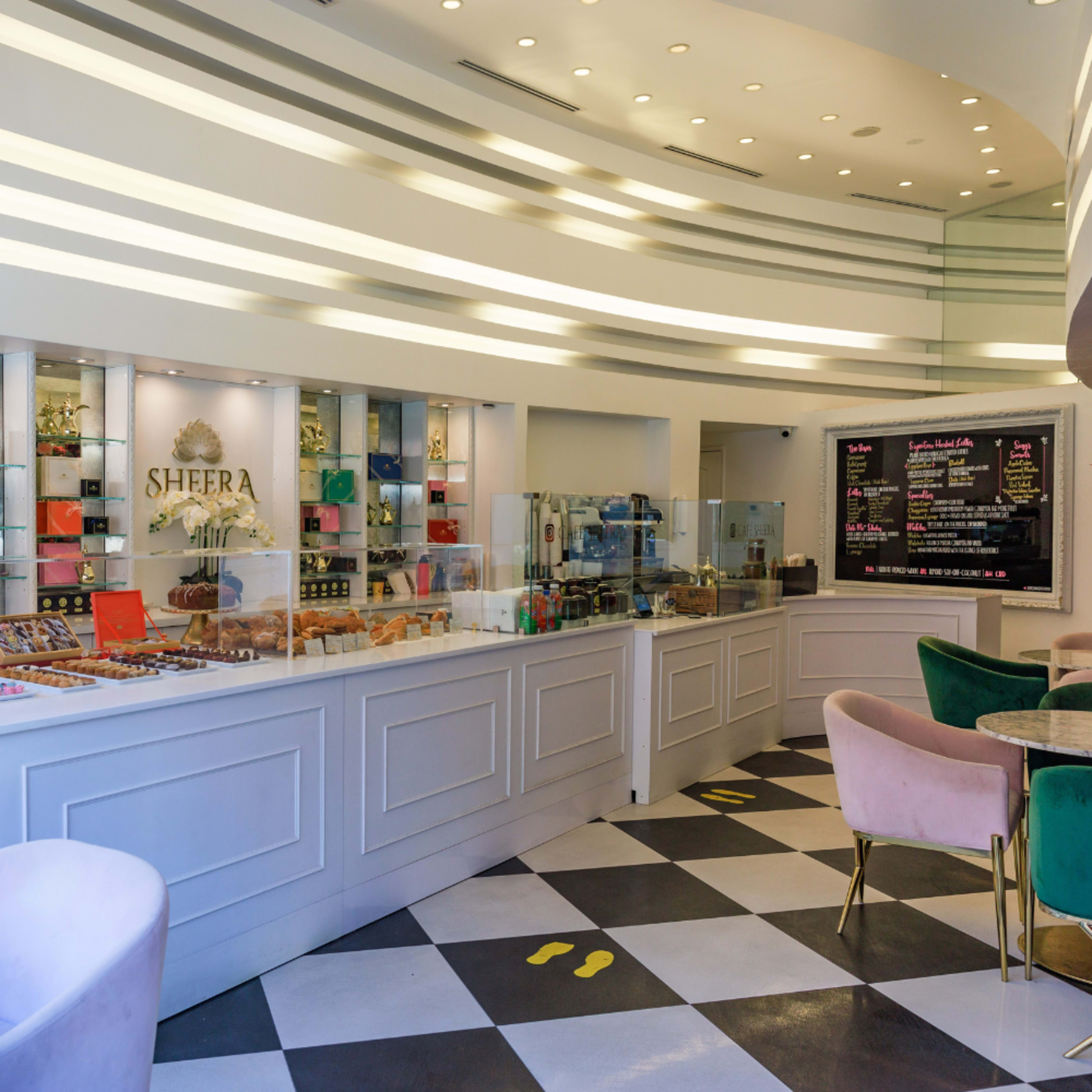 A modern café with a sleek counter displaying various pastries and a large menu board on the wall.