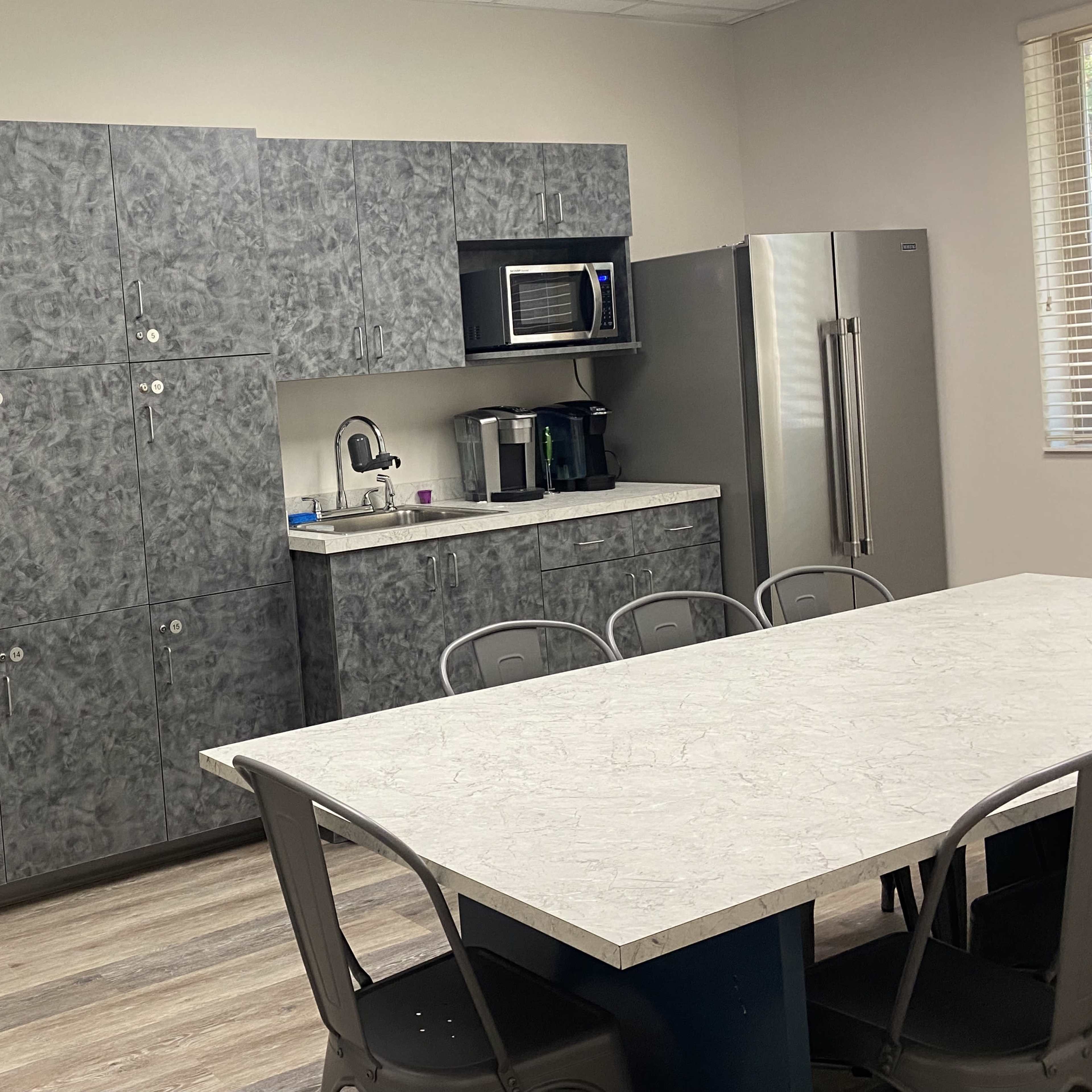 A modern kitchen with gray cabinets, a countertop, a microwave, a coffee maker, and a dining table with metal chairs.