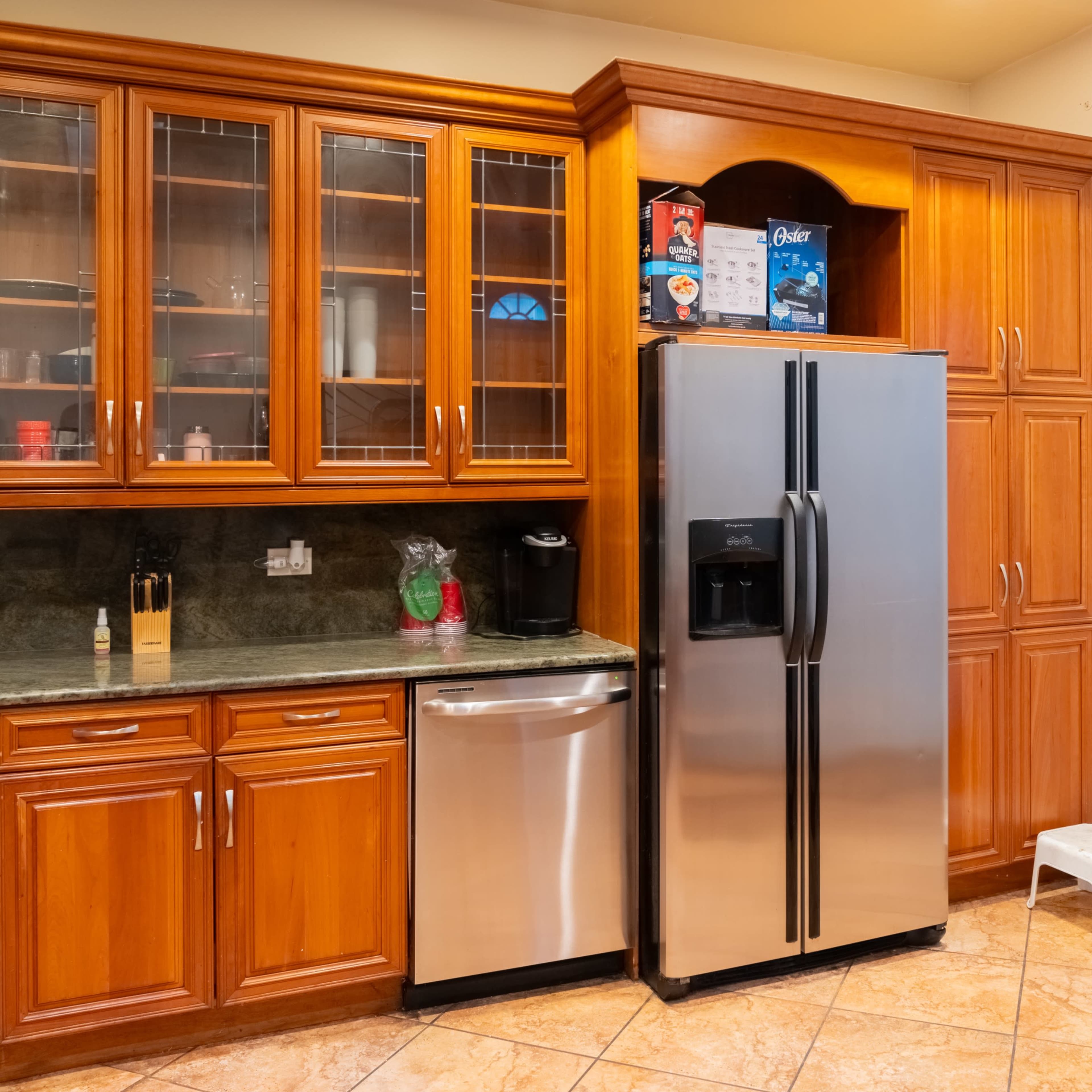 The kitchen features wooden cabinetry, a stainless steel refrigerator, and a countertop with an assortment of kitchen appliances.