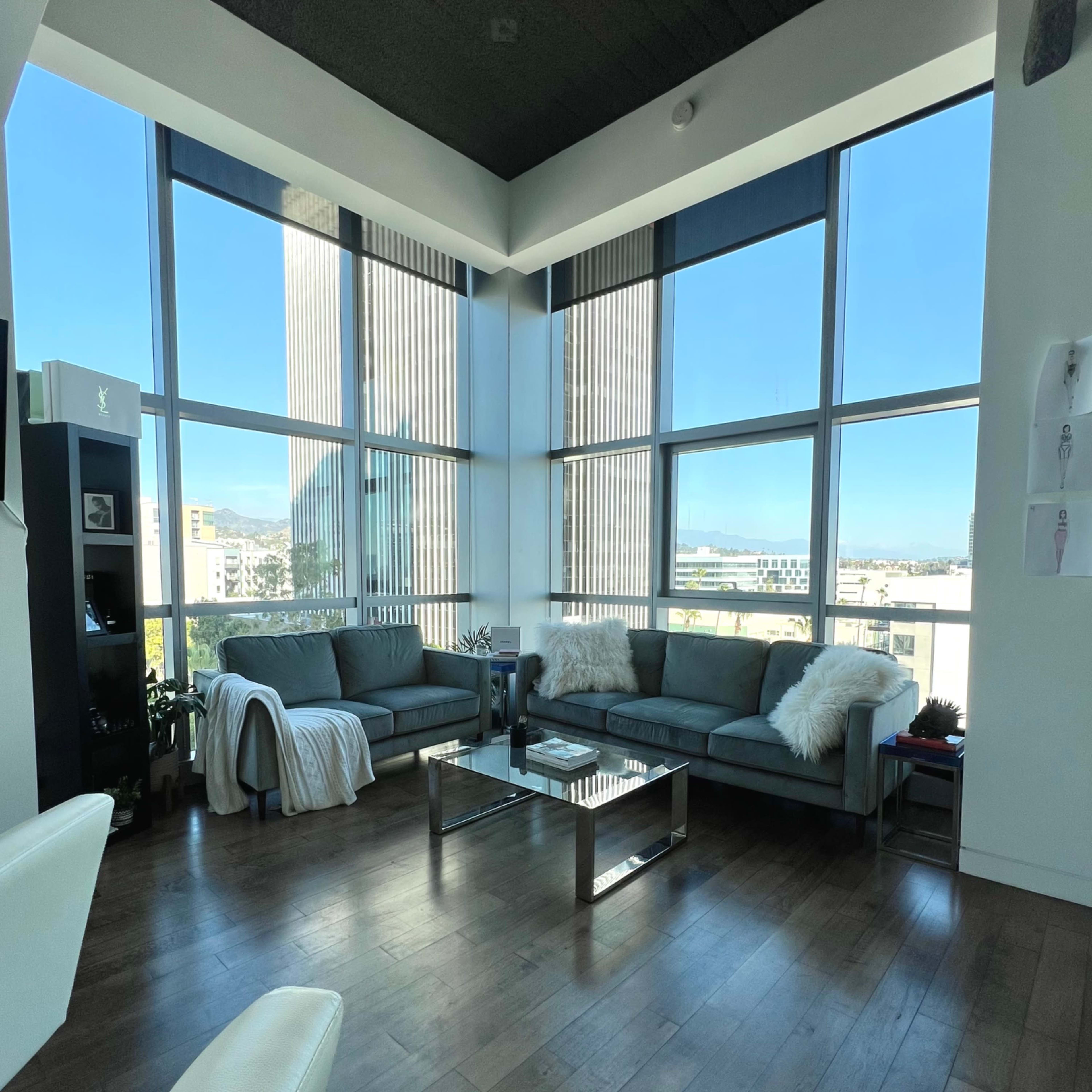 A modern living room features large windows with a view of city buildings, two sofas, a coffee table, and hardwood flooring.
