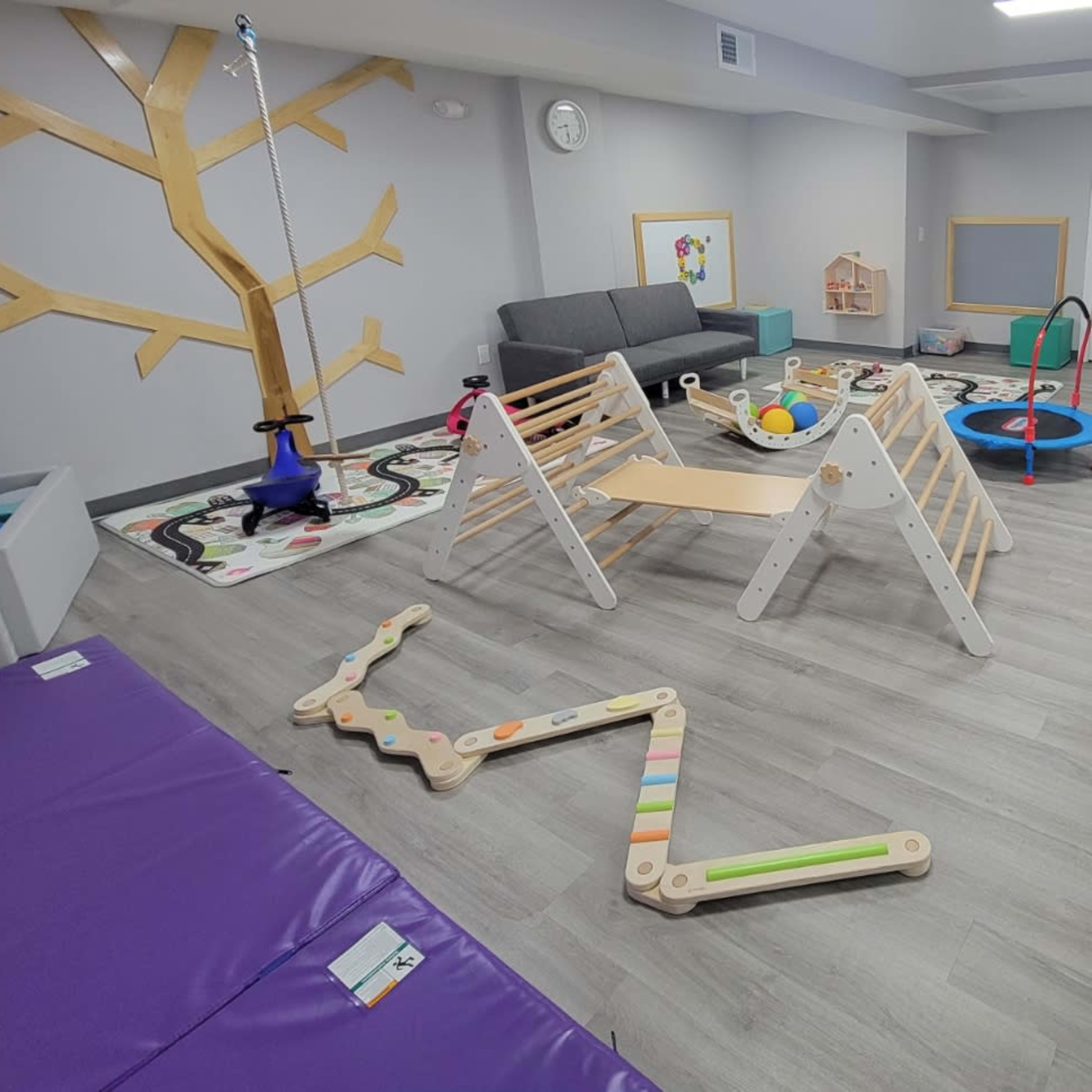 A playroom filled with various children's toys, climbing structures, and colorful mats.