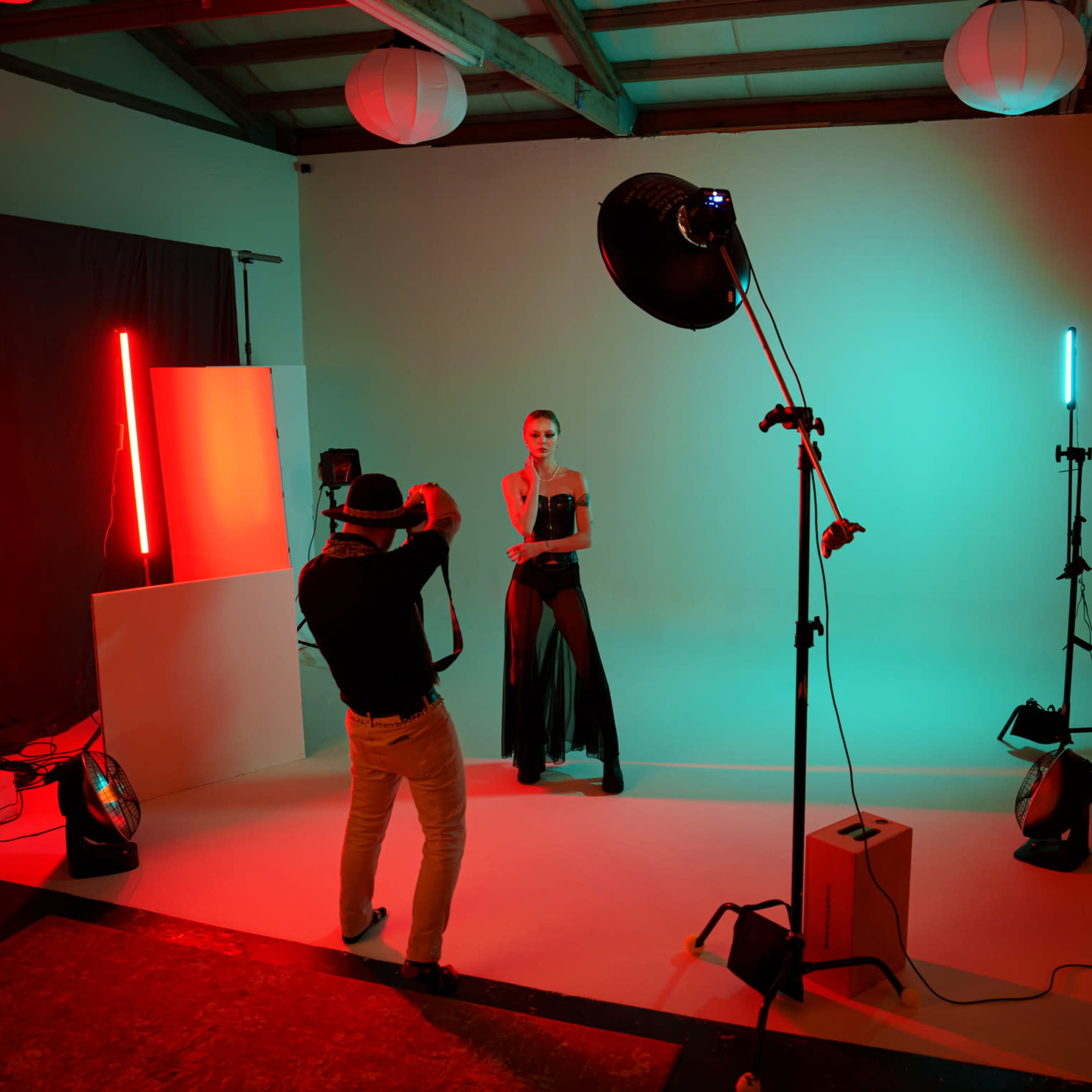 A photographer captures a model posing in a studio lit with colored lights against a neutral backdrop.