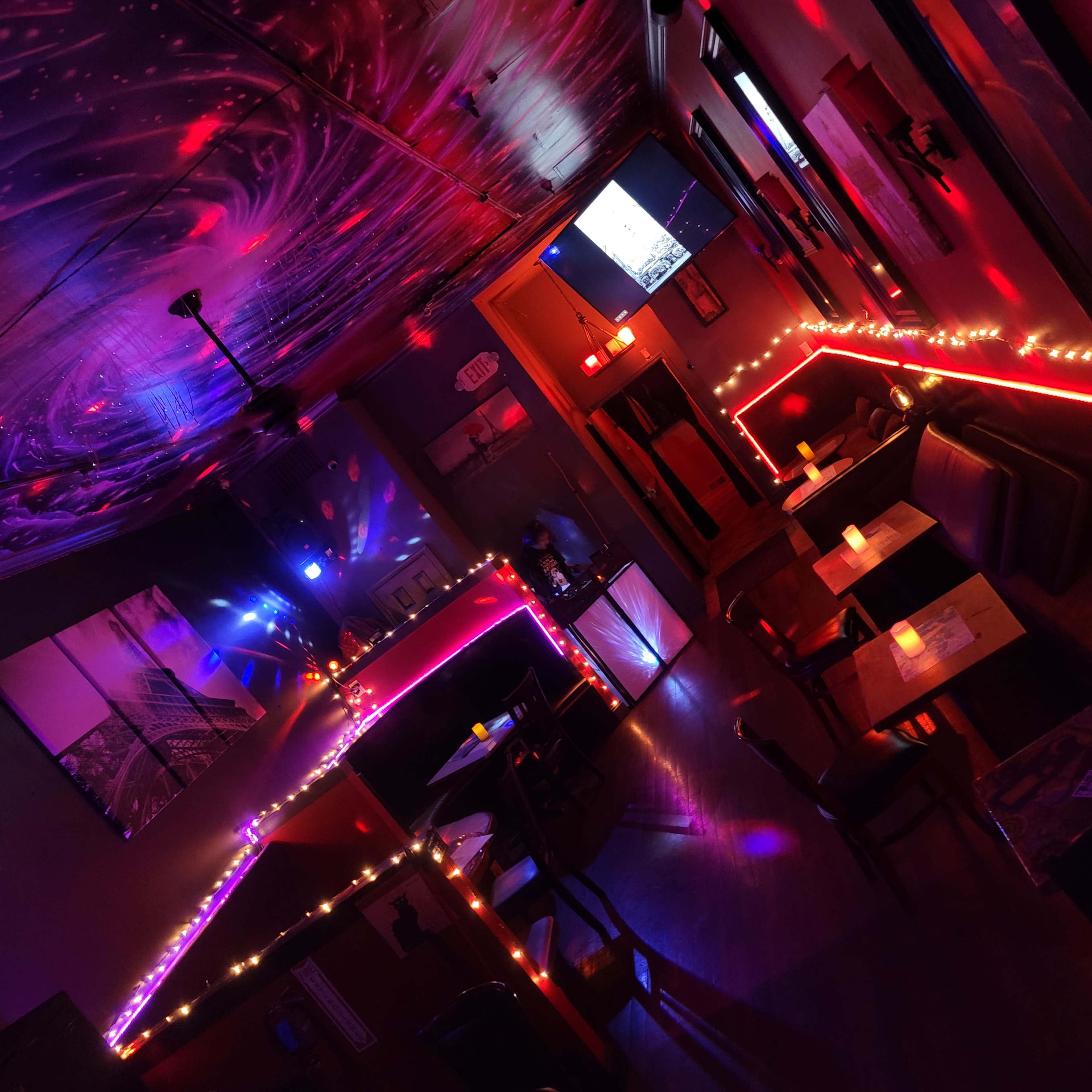 A dimly lit lounge with a swirling ceiling design, colorful lights outlining the seating areas, and candles on the tables.