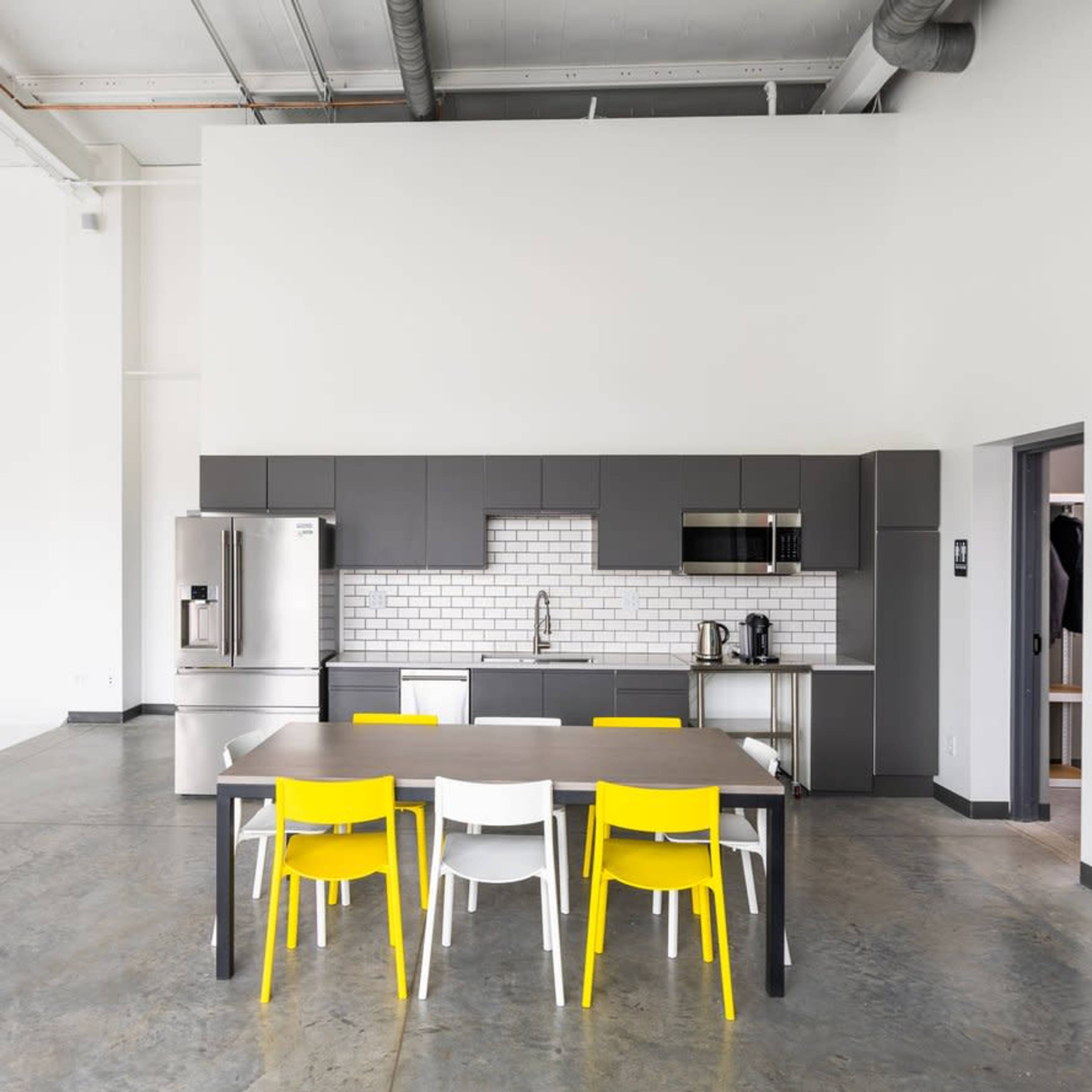 A modern kitchen area with a gray cabinetry, stainless steel appliances, and a table surrounded by yellow and white chairs.
