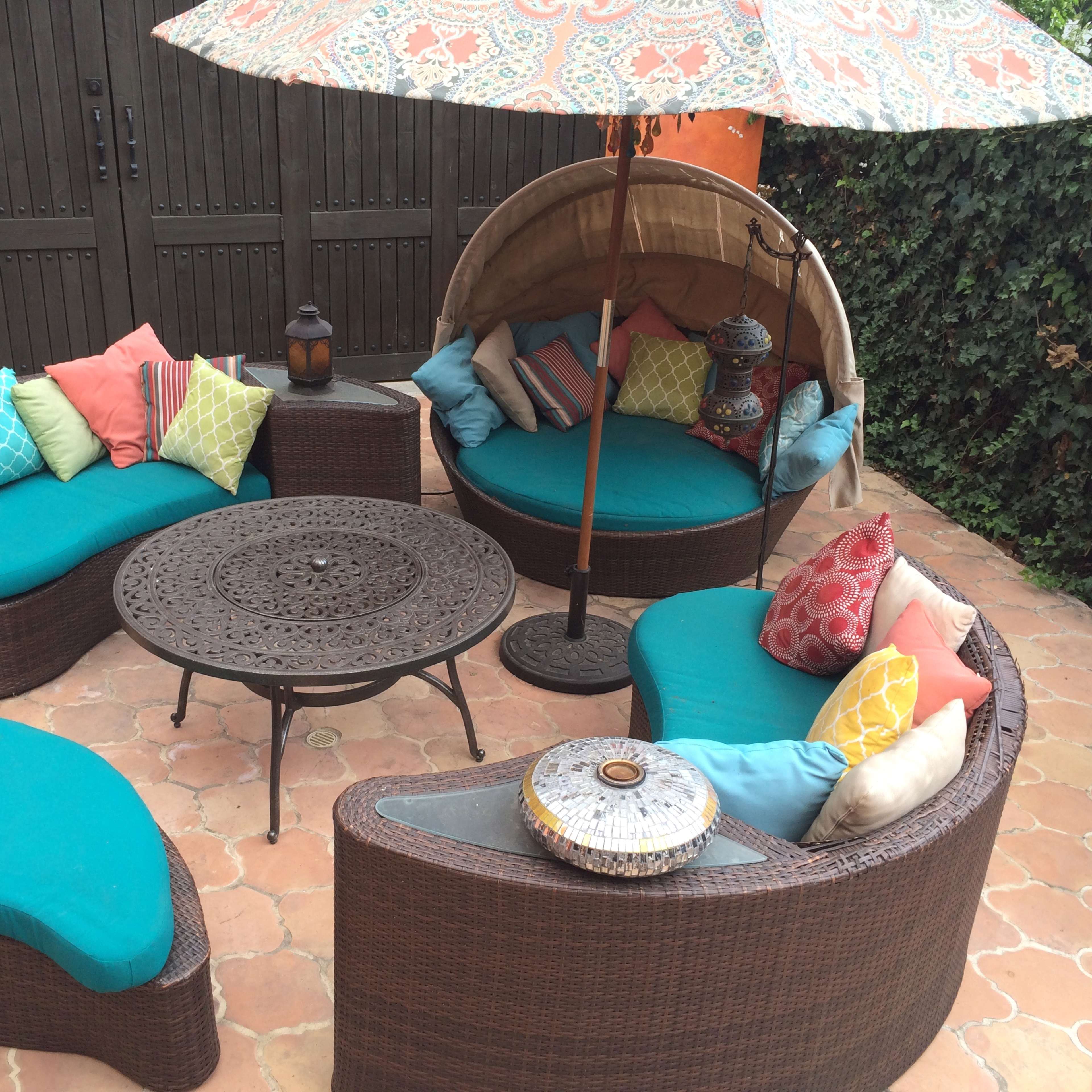 A patio area features a circular seating arrangement with blue cushions, a patterned umbrella, and a decorative table at the center.