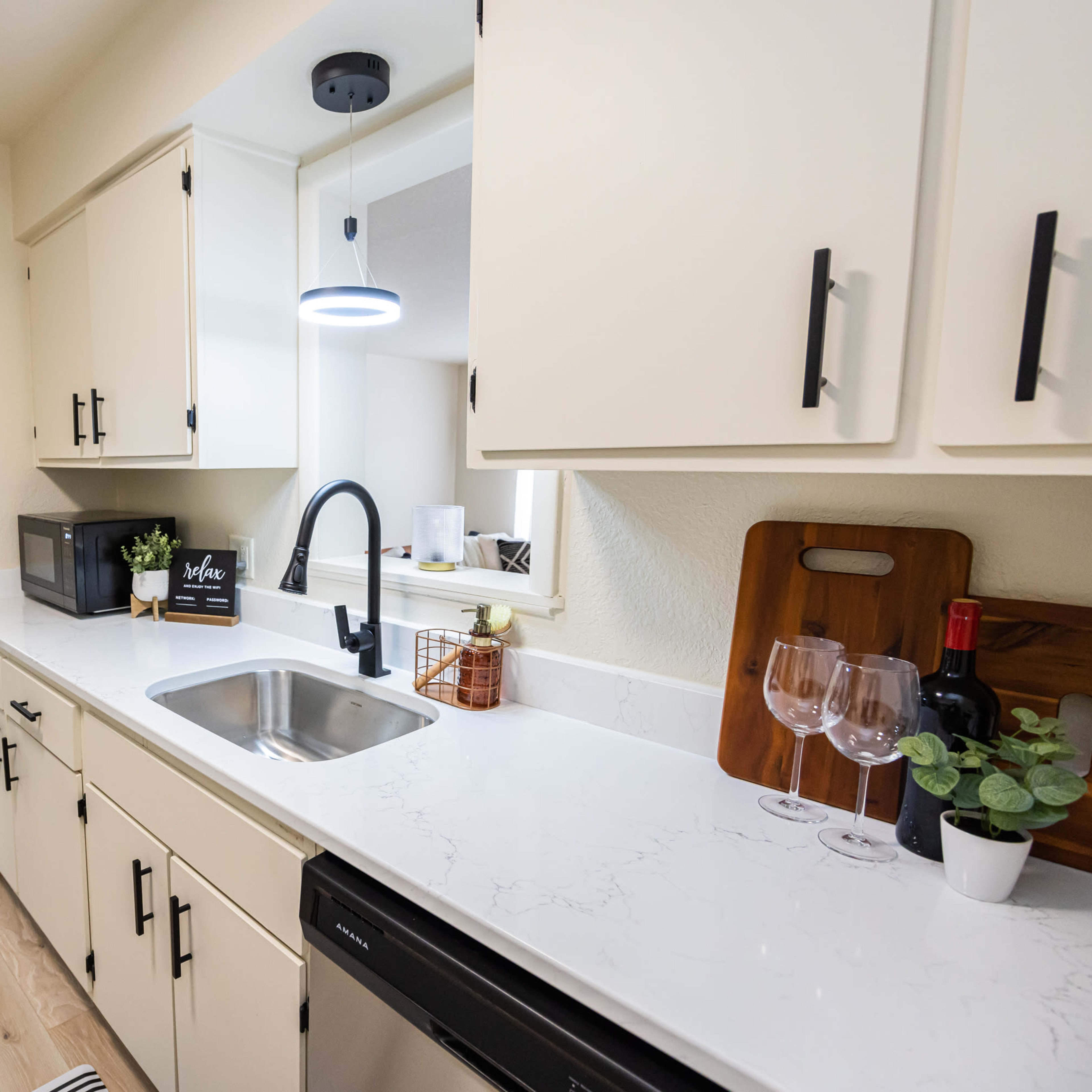 A modern kitchen with white cabinets, a sink, and a countertop, leading to a dining area with a table and chairs visible in the background.