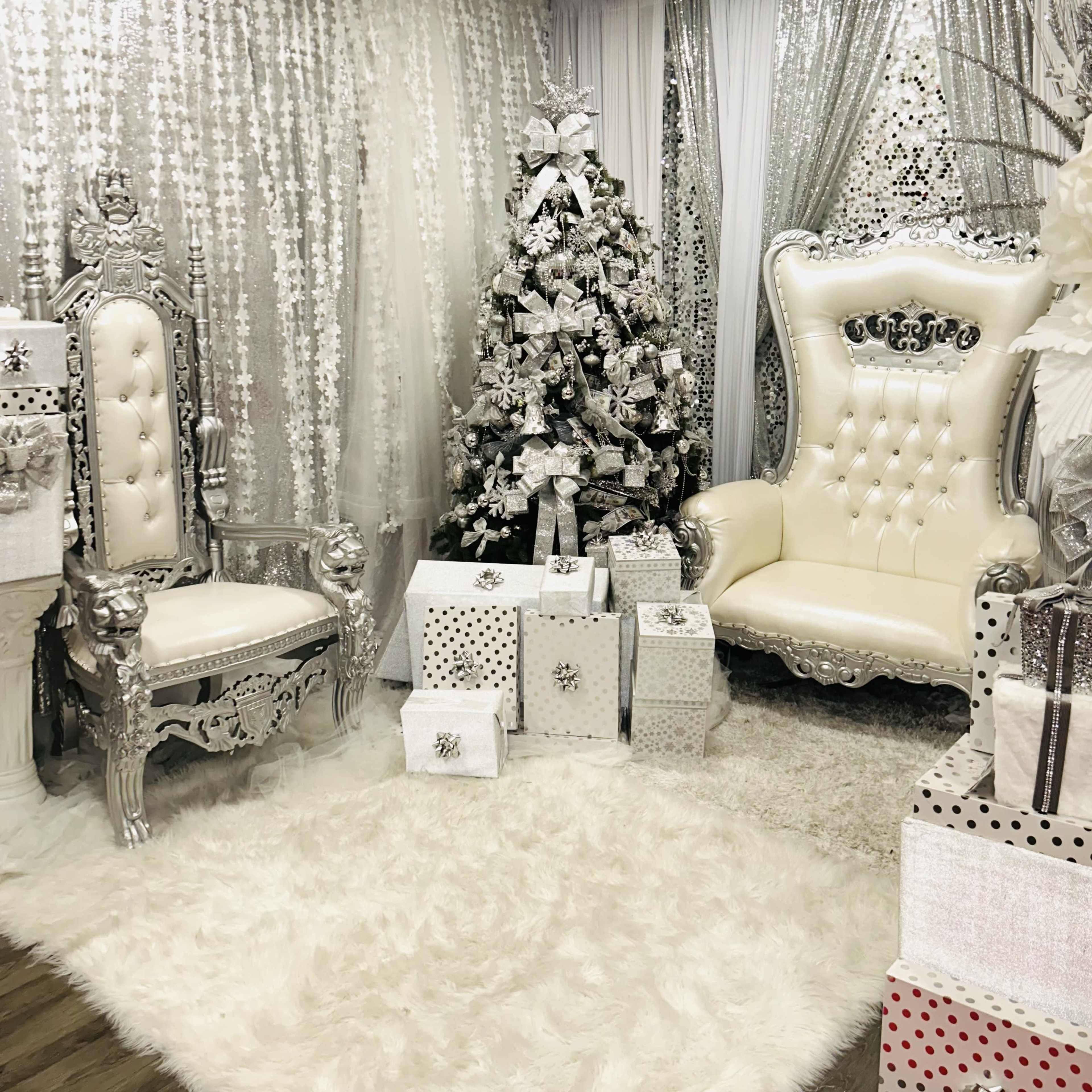 An elegantly decorated room featuring silver and white furniture, a Christmas tree, and wrapped presents.