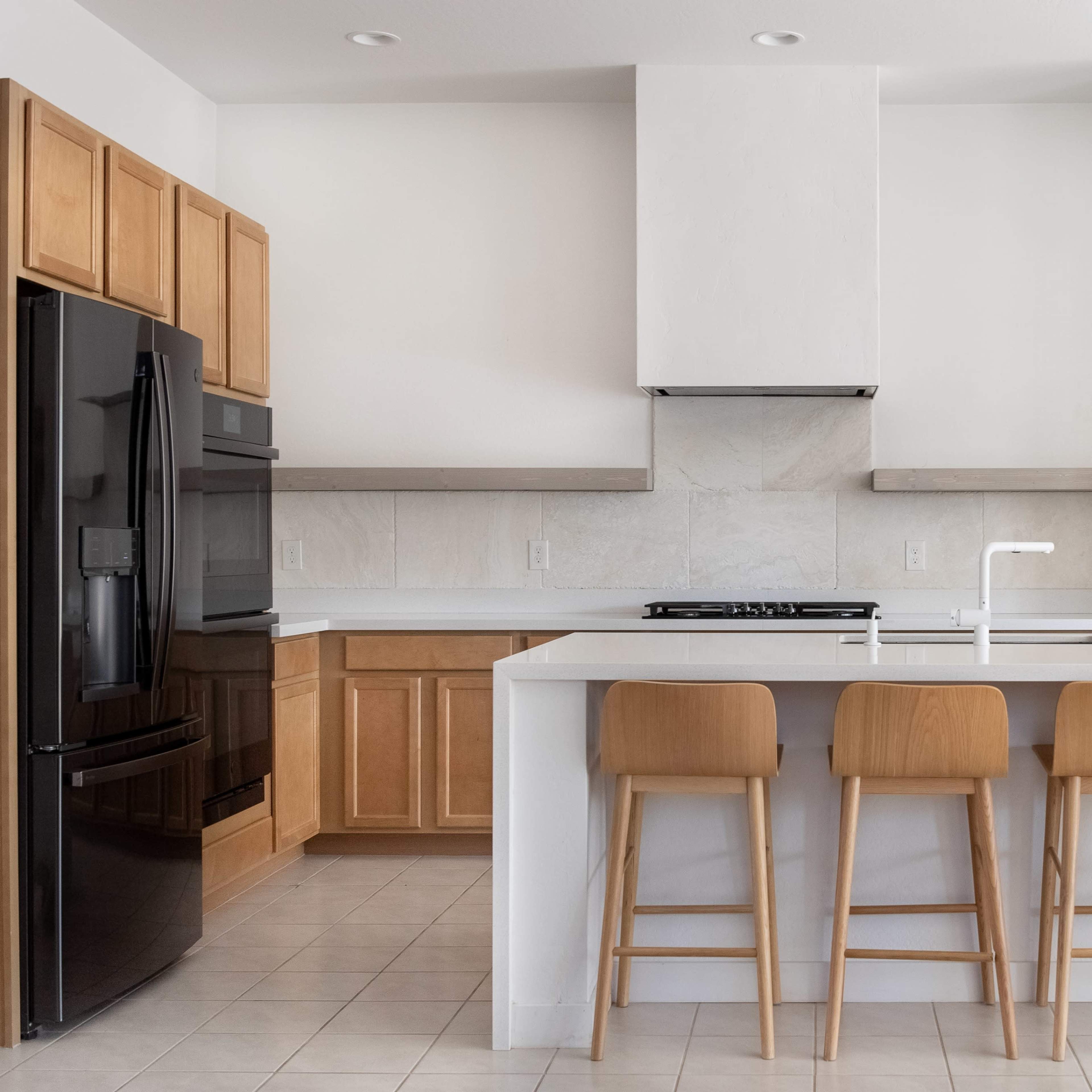 A modern kitchen features wooden cabinets, a black refrigerator, and a white island with four wooden bar stools.