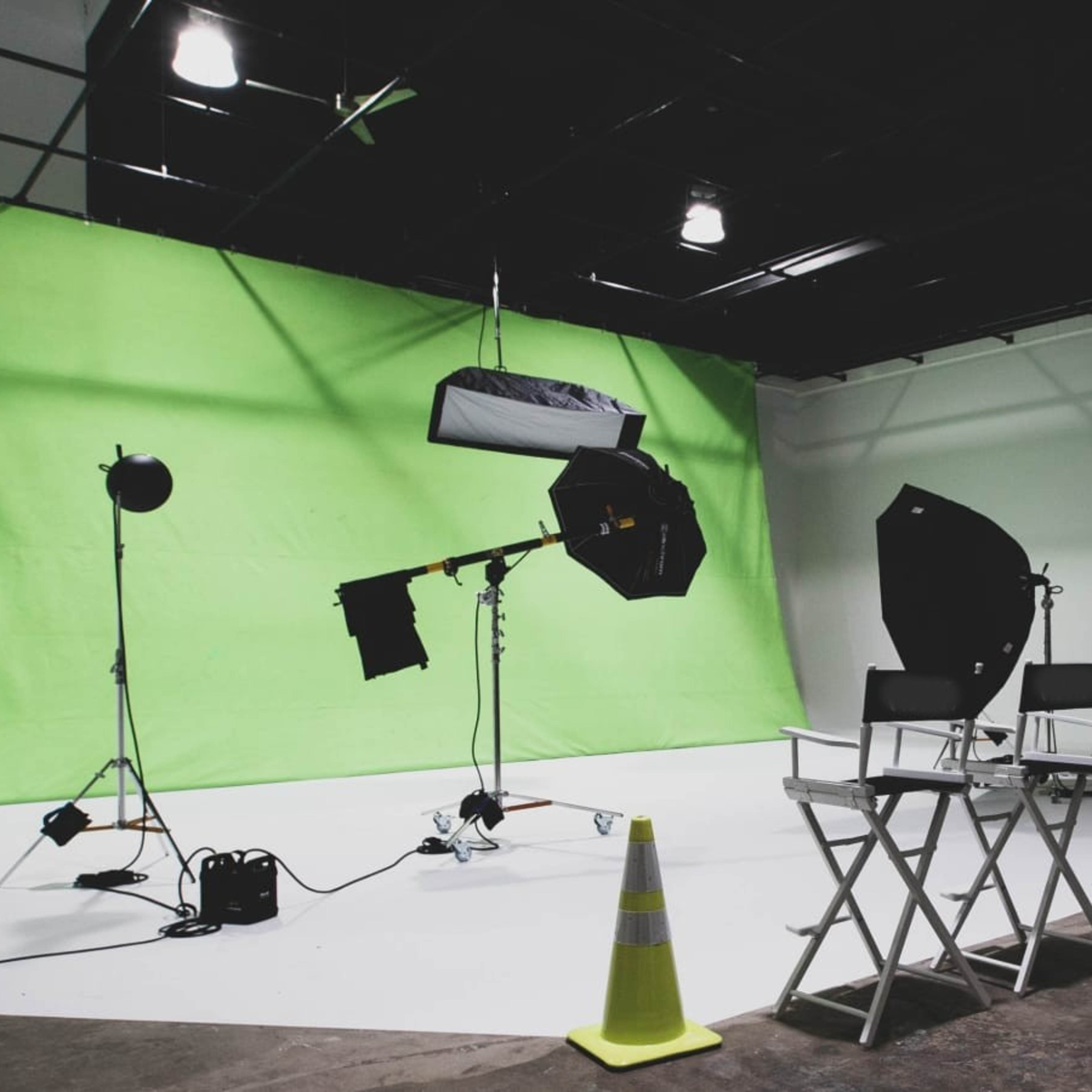A film studio setup with a green backdrop, lighting equipment, and director's chairs positioned for a shoot.