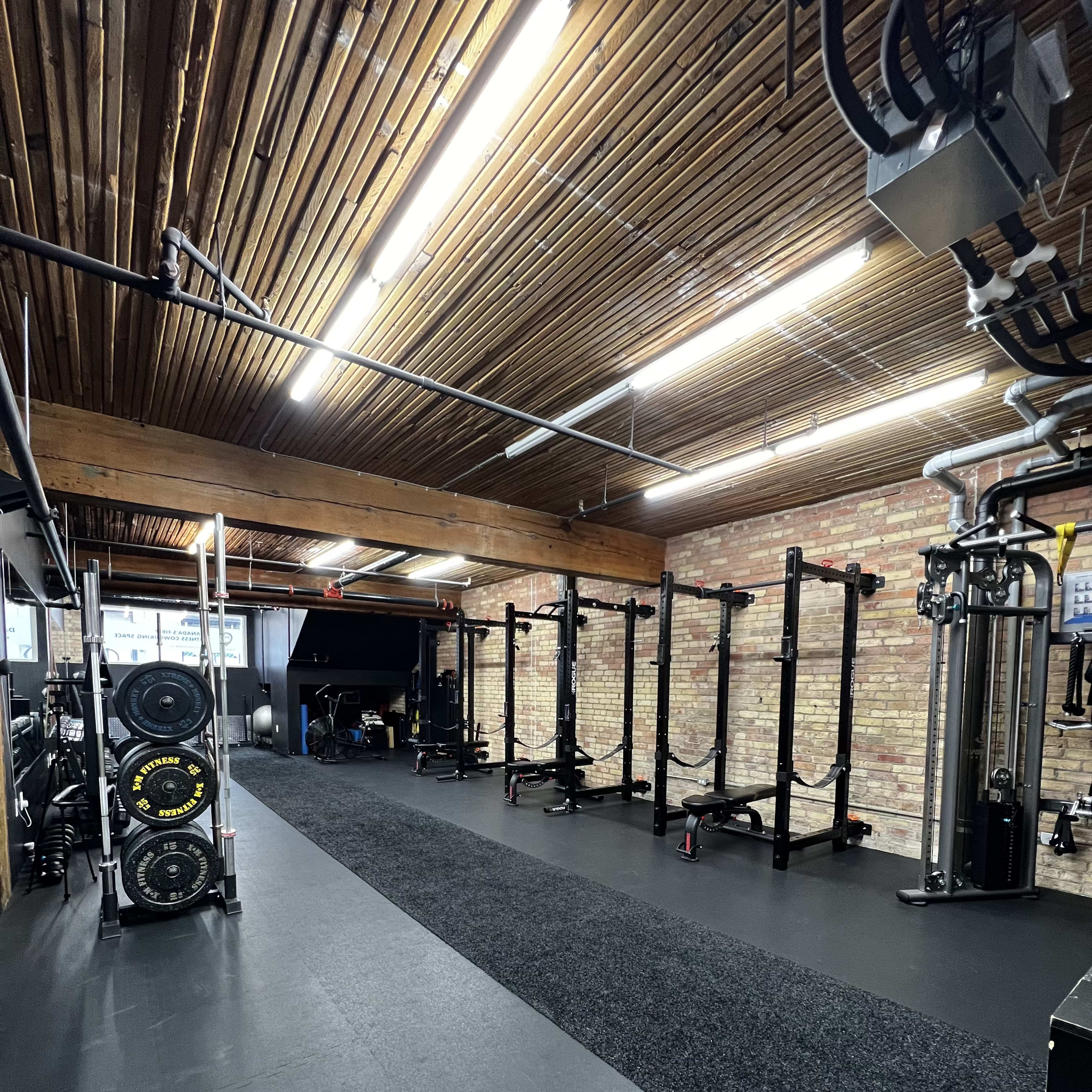 A spacious gym with weightlifting equipment, a black rubber floor, and a wooden ceiling with exposed beams.